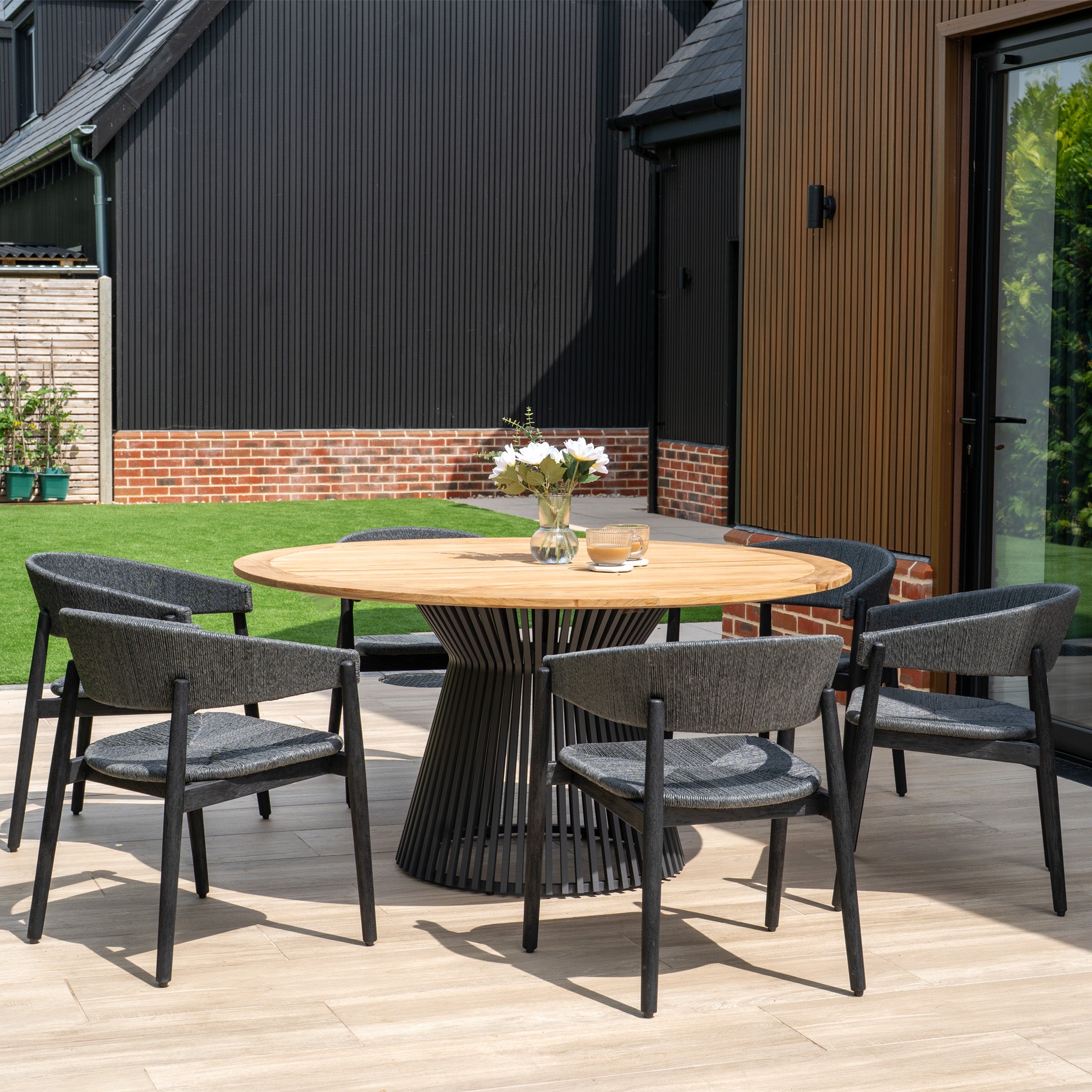 The Lucca 6 Seat Dining Set features a teak round table in black and six stylish chairs, perfect for outdoor patio dining.