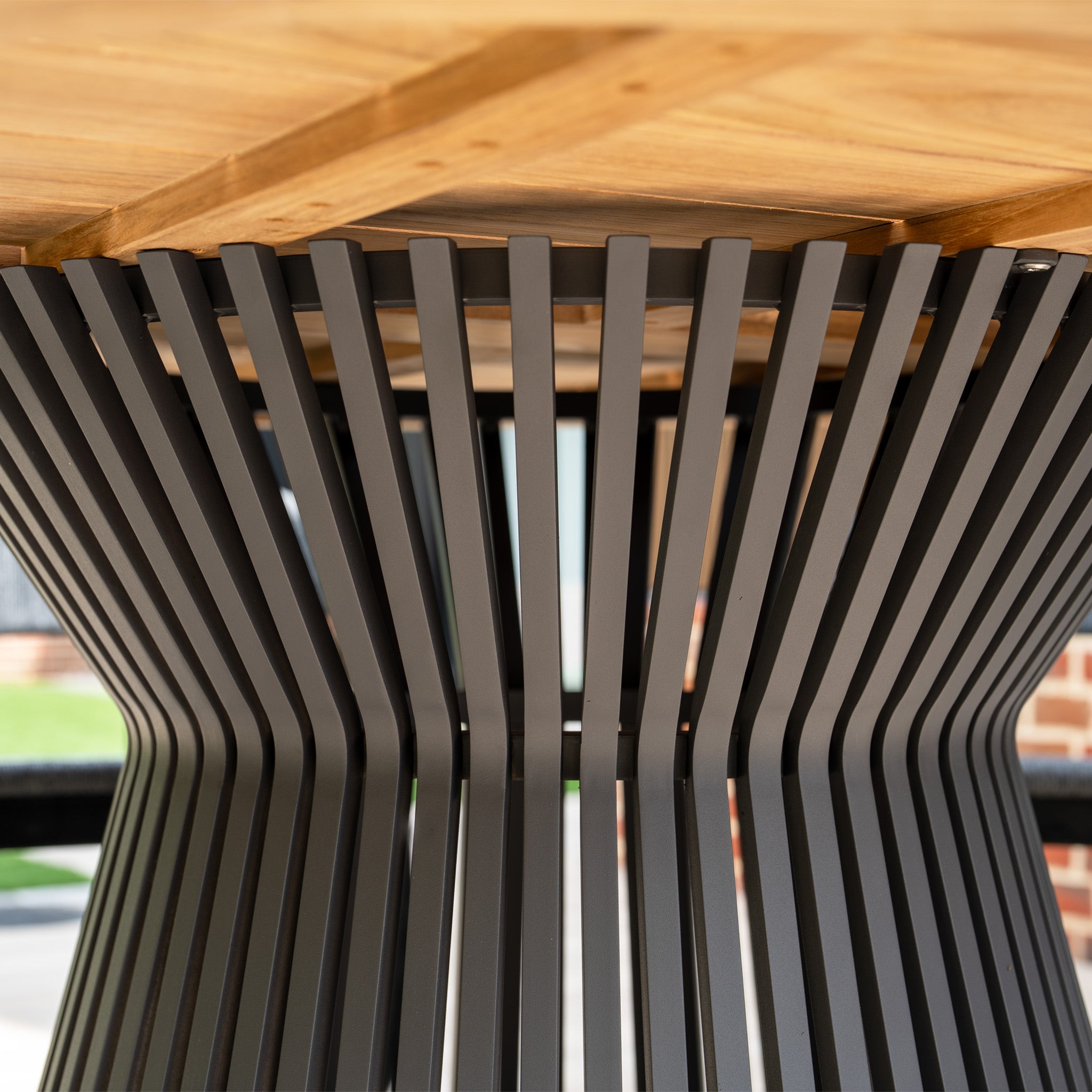 Close-up of the Lucca 6 Seat Dining Set featuring a teak round table with a wooden top and black metal slat base, ideal for outdoor dining.