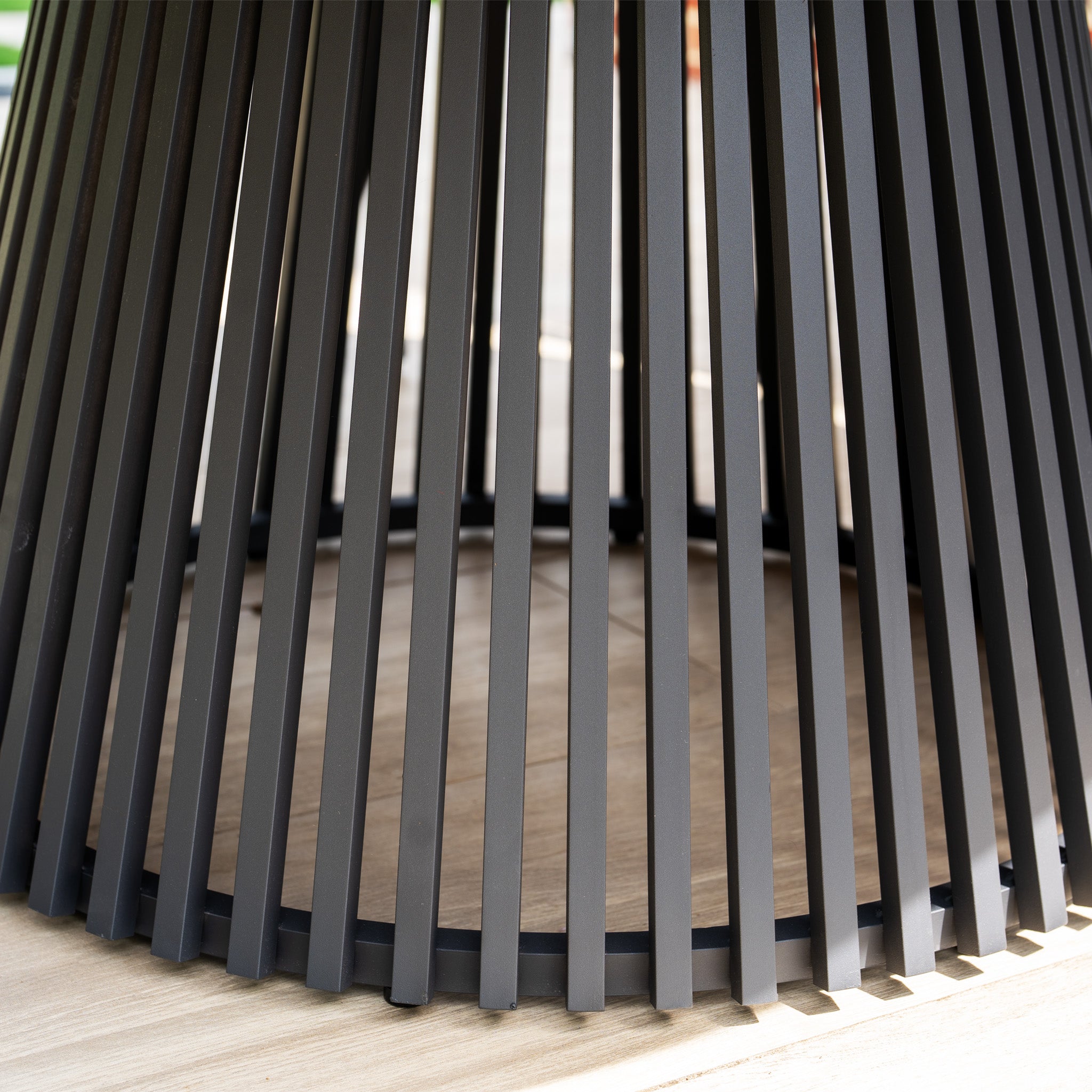 Close-up of black metal slats shaping a circular, open base on light wood flooring—an elegant detail from the Lucca 6 Seat Dining Set with Teak Round Table in Black.