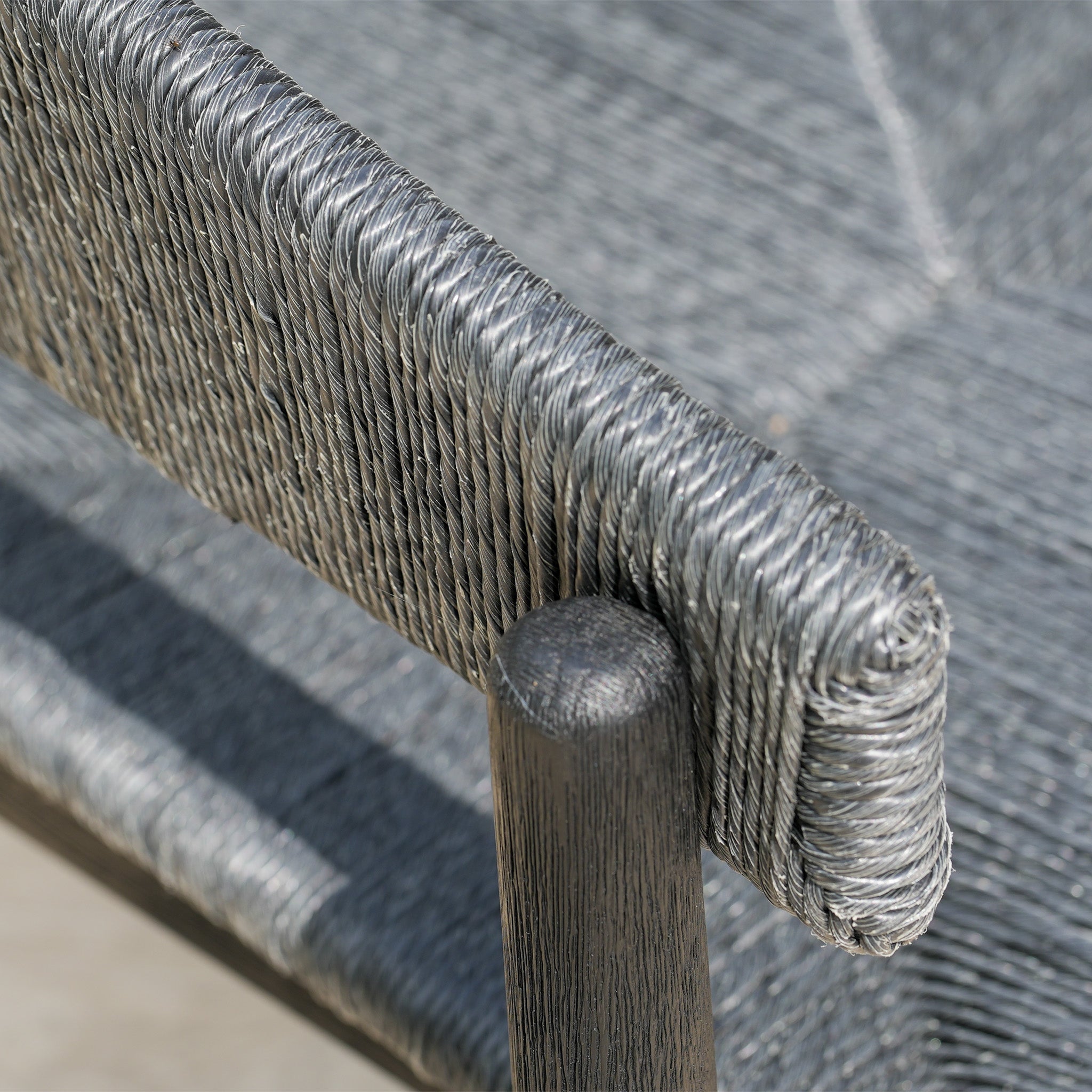 Close-up of a chair featuring a tightly woven gray rope seat and backrest with a dark wooden frame—ideal for pairing with the Lucca 6 Seat Dining Set with Teak Round Table in Black.