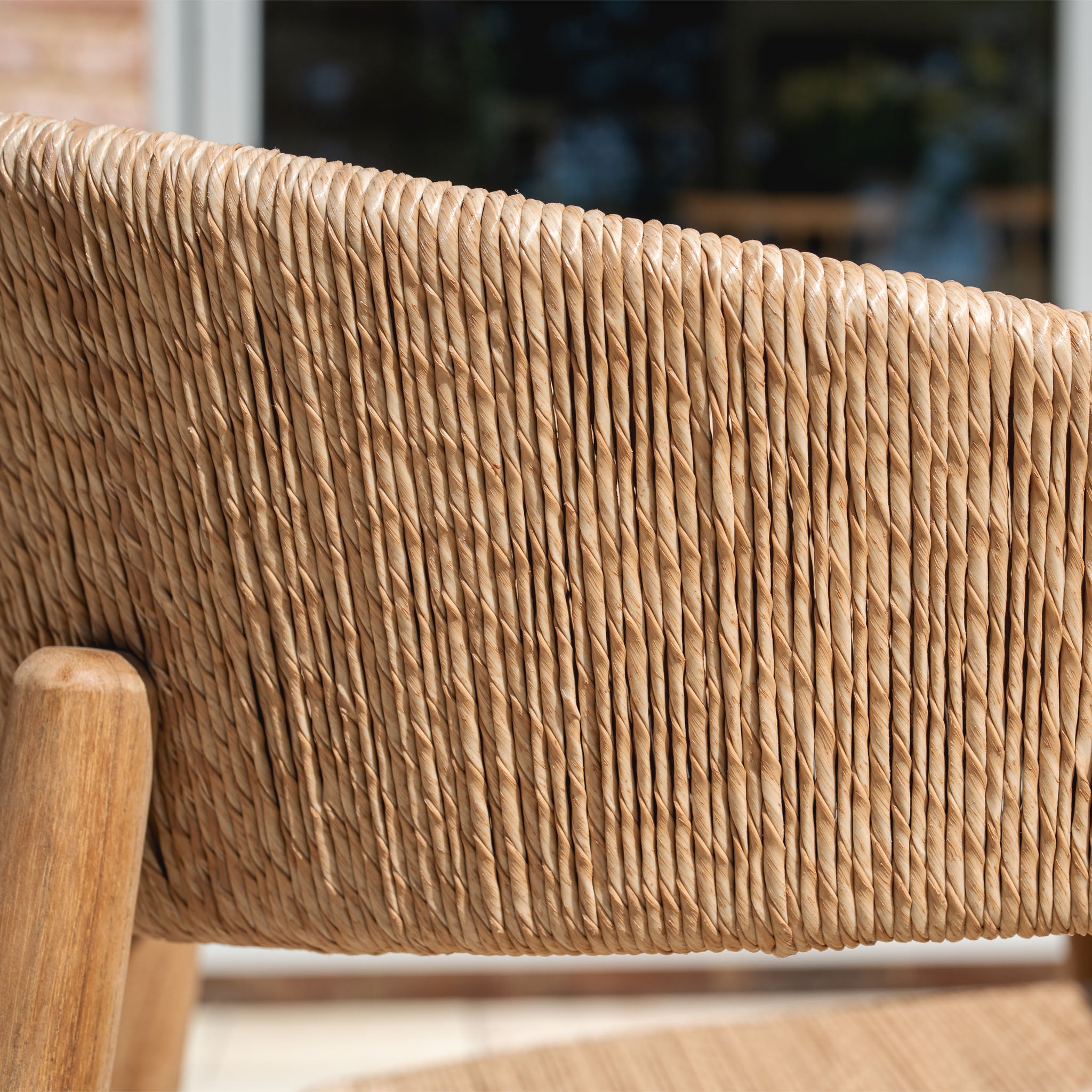 Close-up of a woven rattan chair backrest with a wooden frame, part of the Lucca 8 Seat Dining Set with Ceramic Top Table in Natural Weave, shown outdoors in natural light.