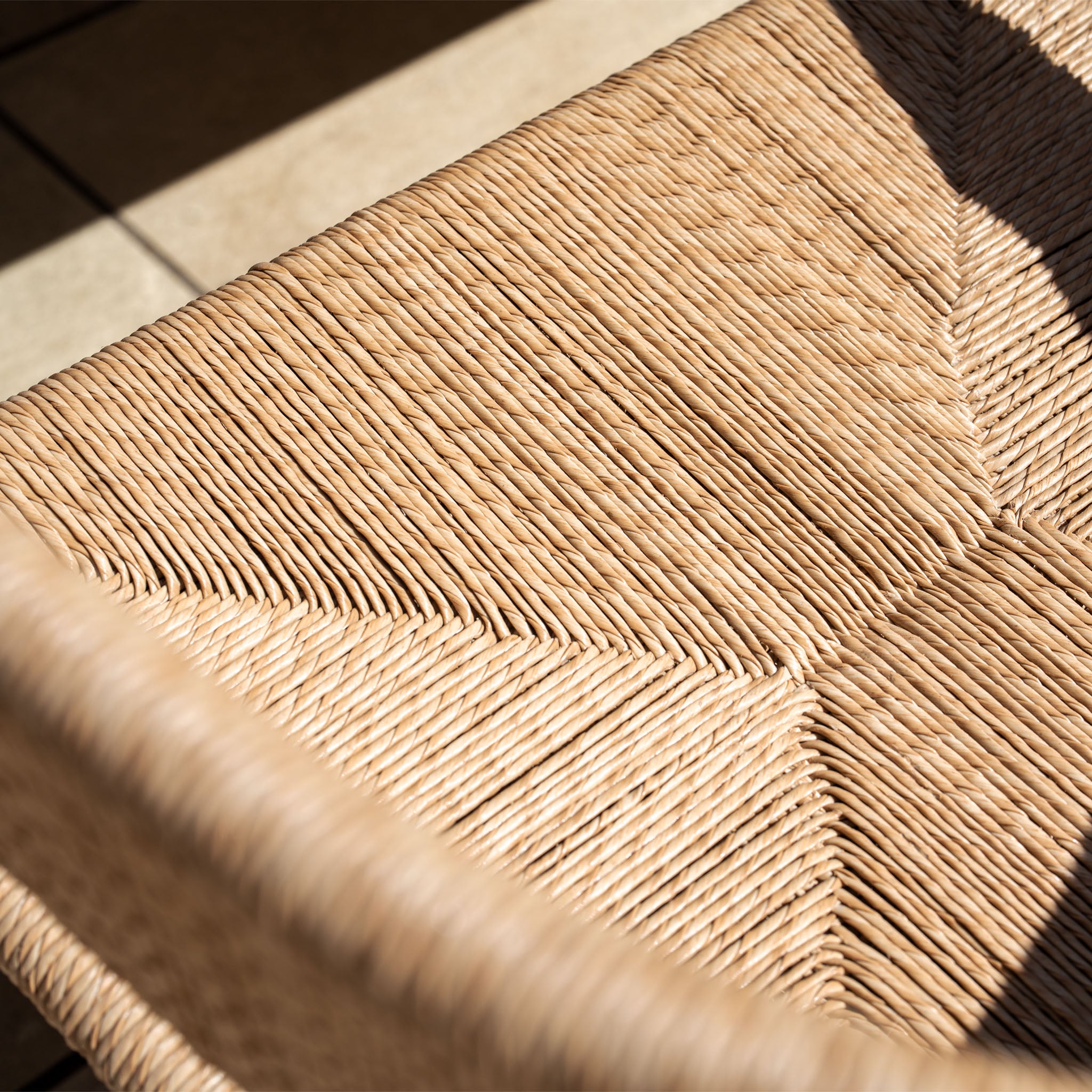 Close-up of the woven rattan seat from the Lucca 8 Seat Dining Set with Ceramic Top Table in Natural Weave, highlighting detailed texture and sunlit shadows—an ideal addition to your outdoor dining space.