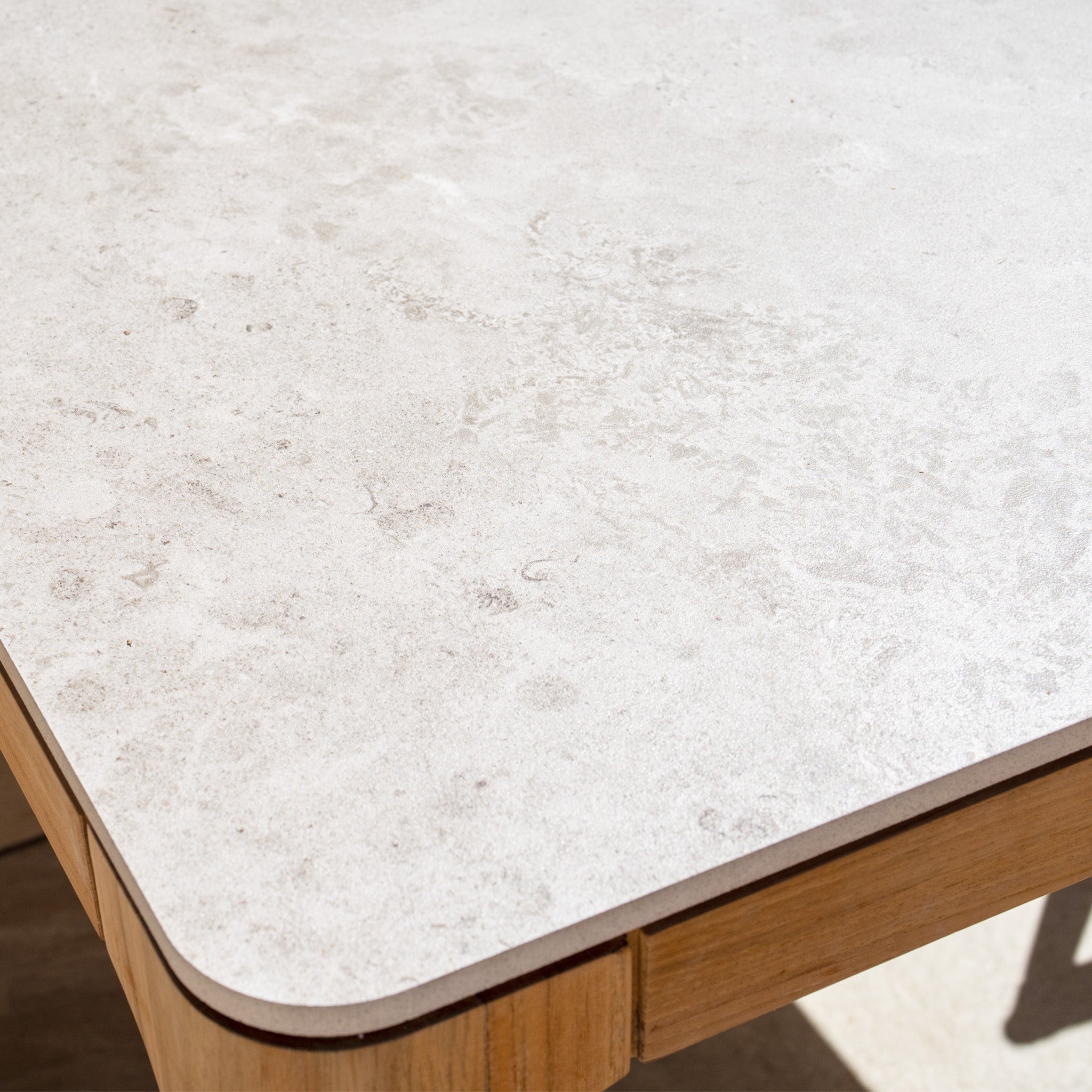 Close-up of the ceramic table top with wooden edge featured in the Lucca 8 Seat Dining Set with Ceramic Top Table in Natural Weave—an elegant addition to your outdoor furniture collection, shown here in bright sunlight.