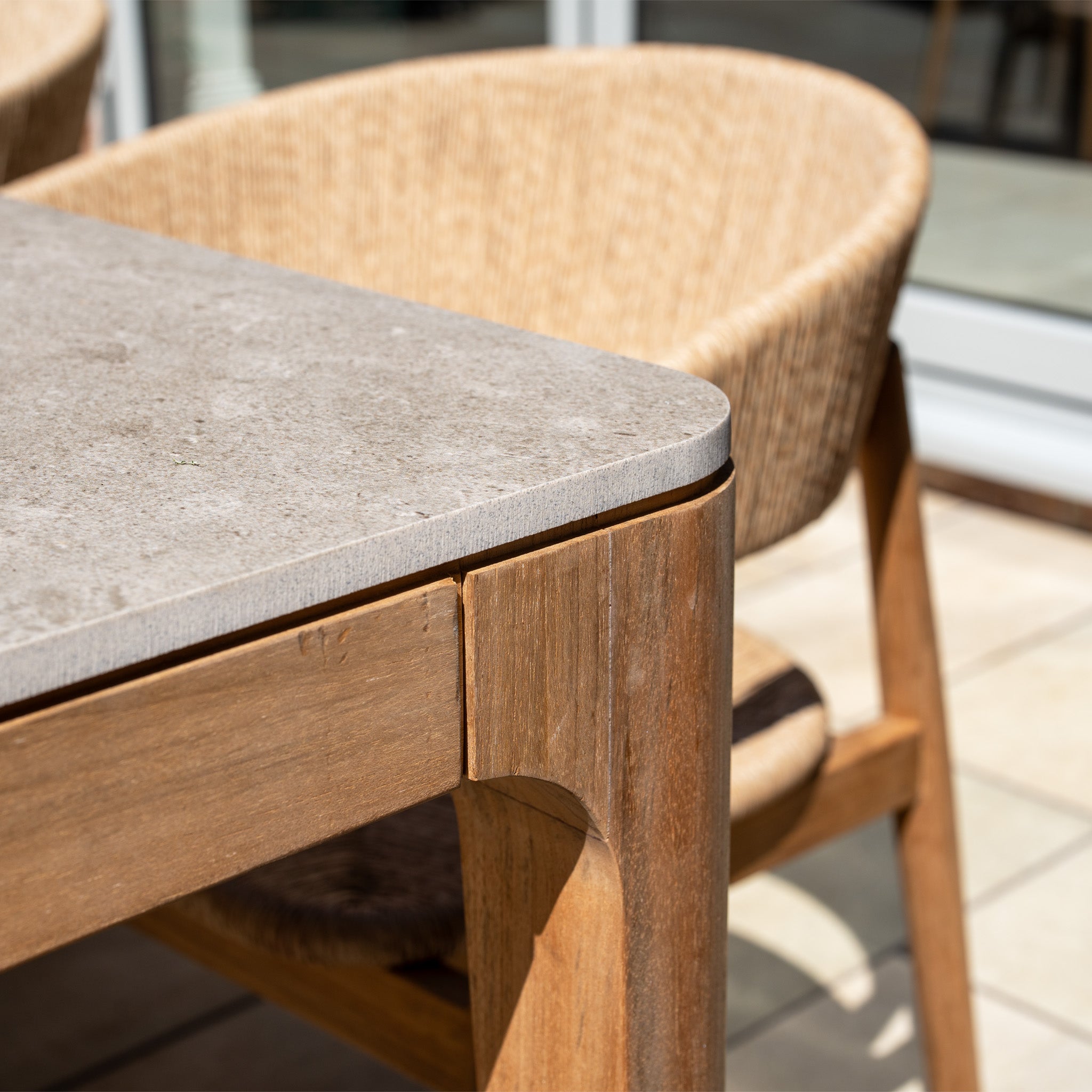 Close-up of the Lucca 8 Seat Dining Set with Ceramic Top Table in Natural Weave, showing its ceramic-topped wooden table and woven chair on a sunny patio.