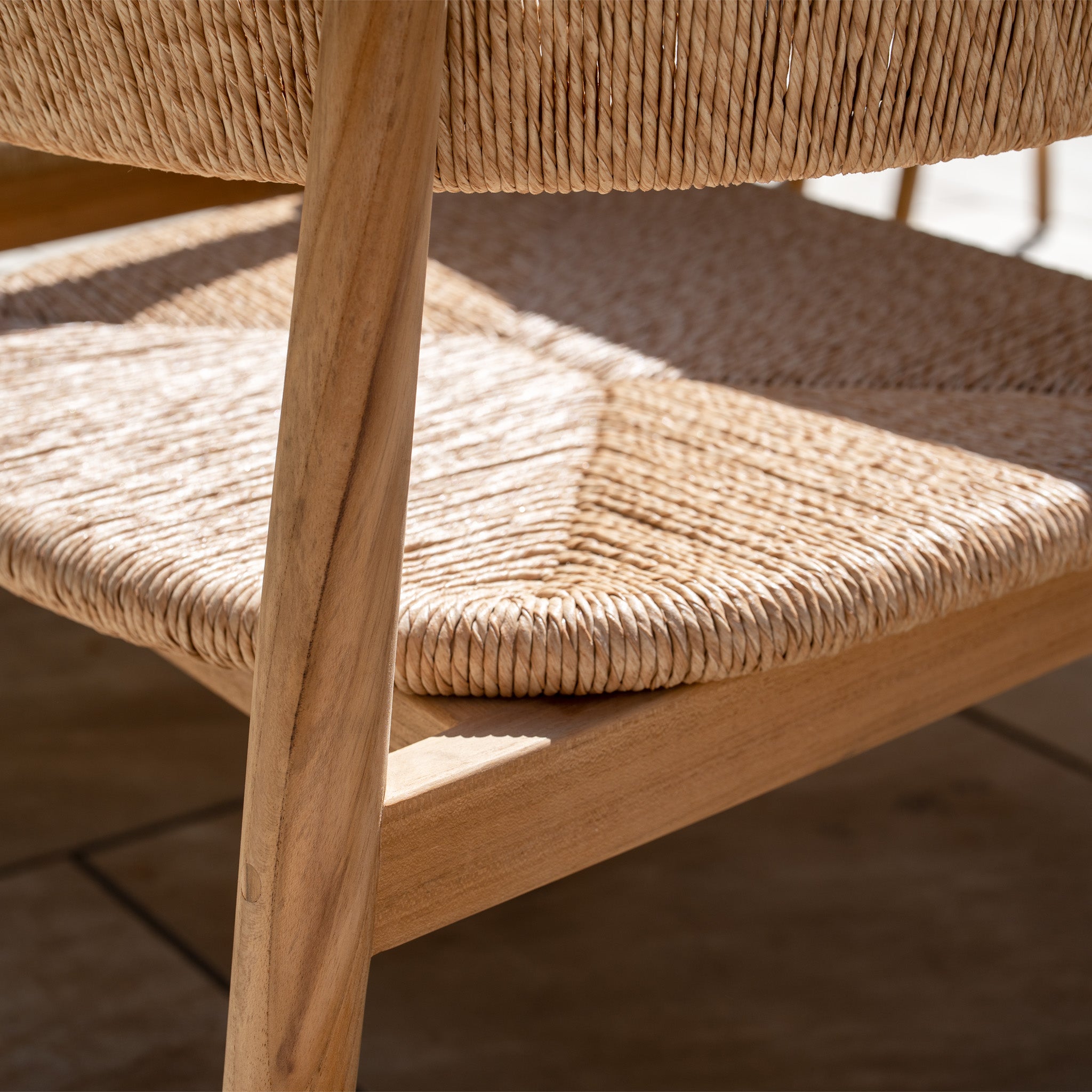 Close-up of a woven rattan chair seat from the Lucca 8 Seat Dining Set with Ceramic Top Table in Natural Weave, sunlight casting elegant shadows—highlighting the beauty of this outdoor furniture.