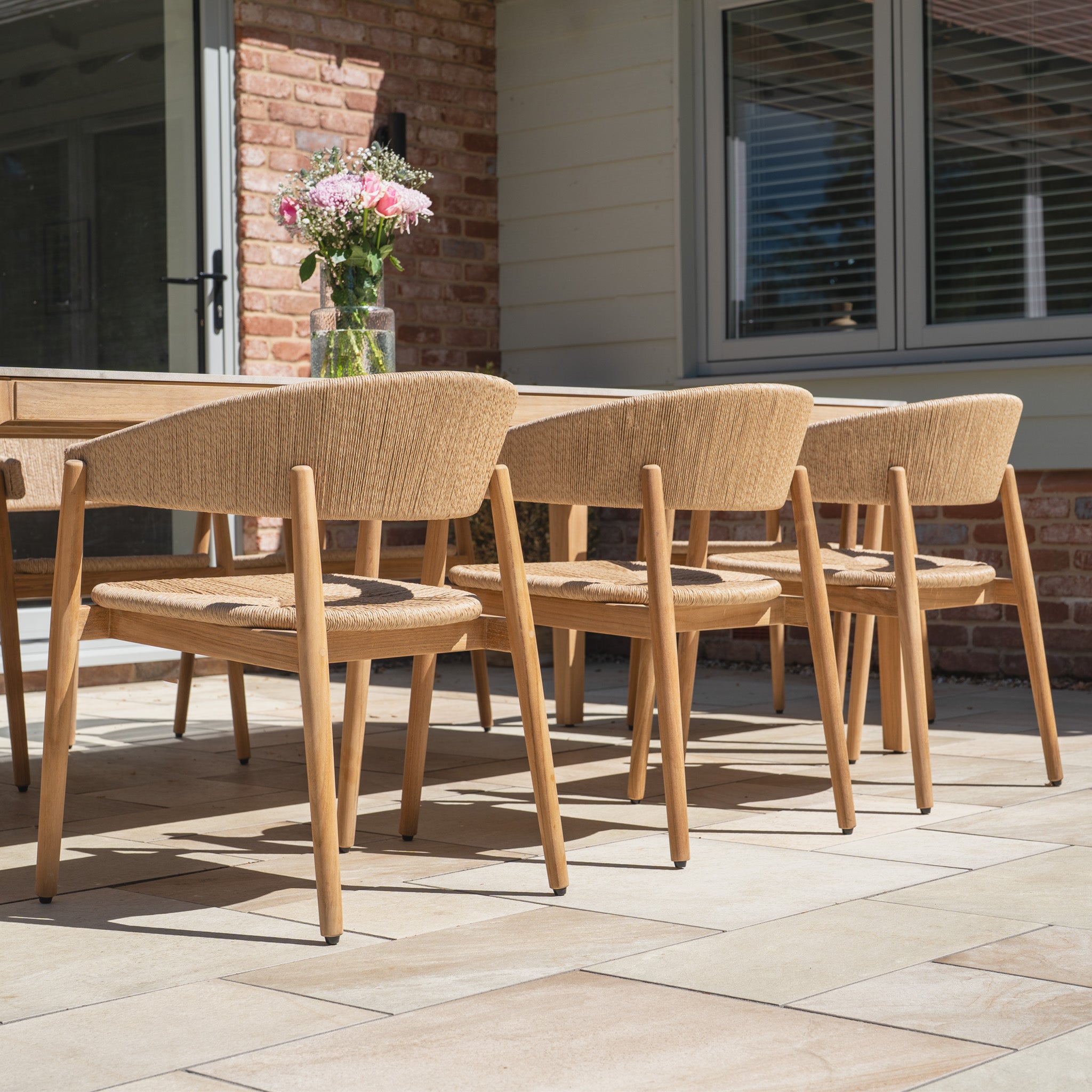 The tiled patio outside the house features the Lucca 8 Seat Dining Set with Ceramic Top Table in Natural Weave, creating inviting outdoor furniture perfect for gatherings.