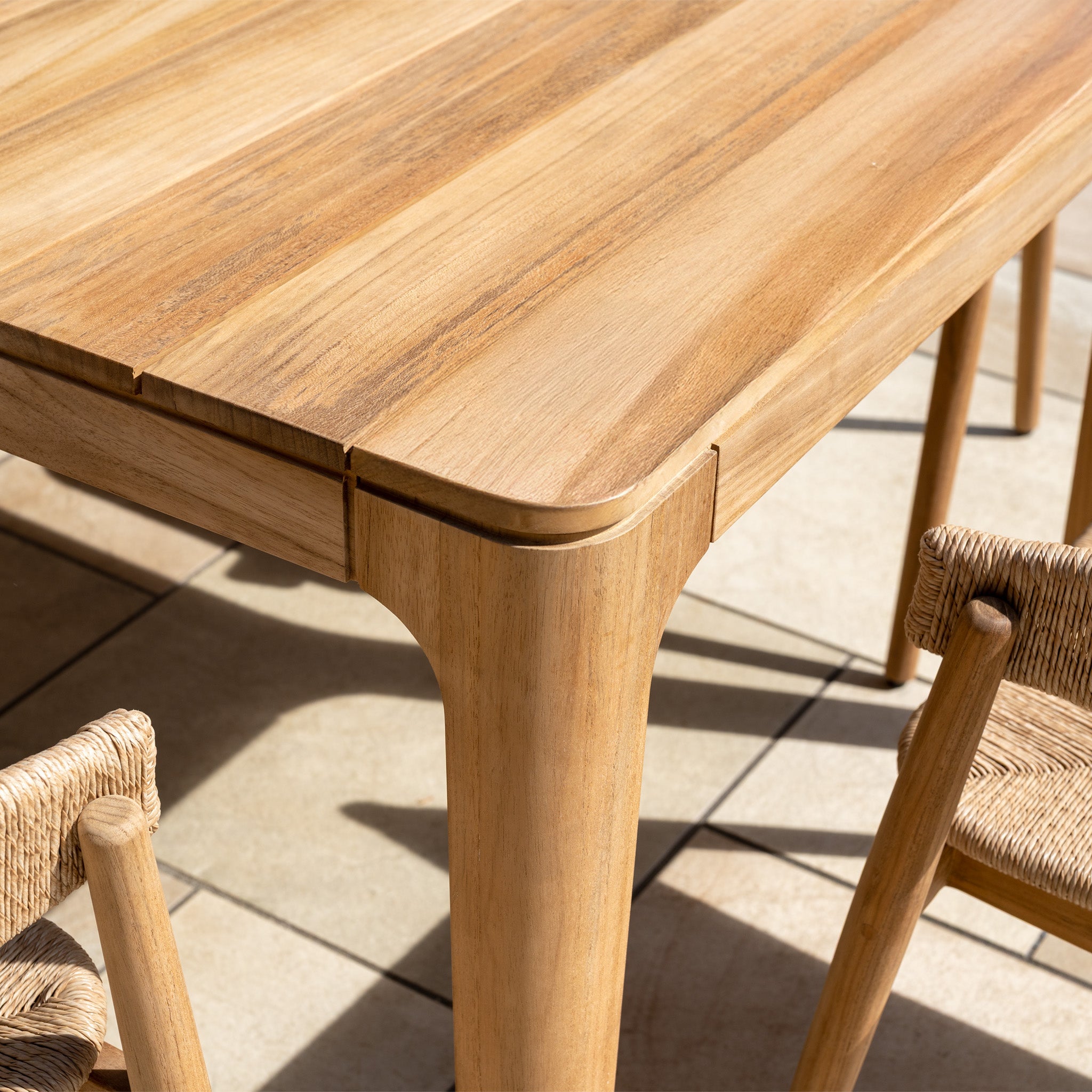 Close-up of the Lucca 8 Seat Dining Set with Teak Table in Natural Weave—rounded edges and woven seats add style to outdoor settings, arranged on a tiled floor.
