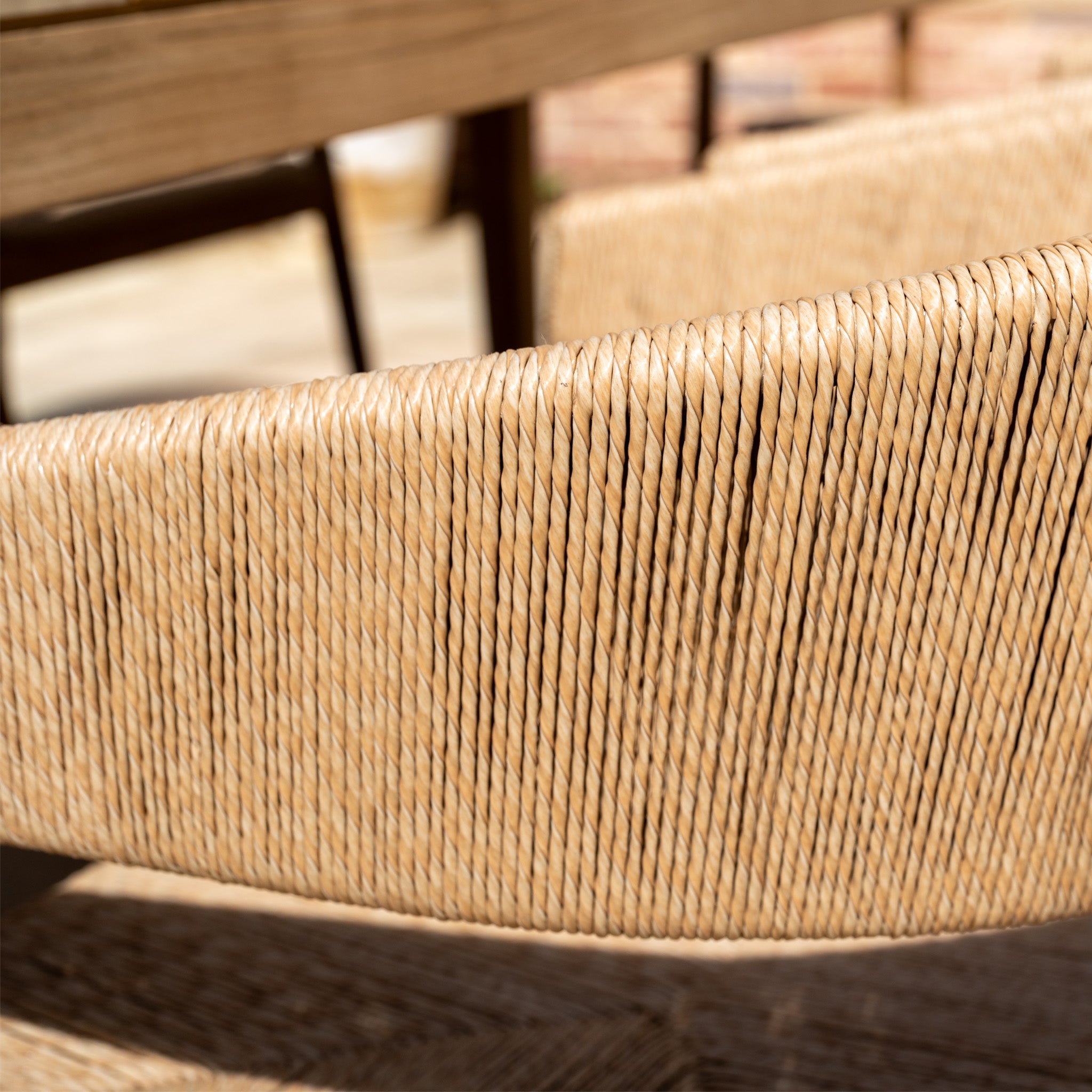 Close-up of a woven rattan chair from the Lucca 8 Seat Dining Set with Teak Table in Natural Weave, sunlight casting shadows on its curved backrest and seat—ideal outdoor furniture for relaxing alfresco.