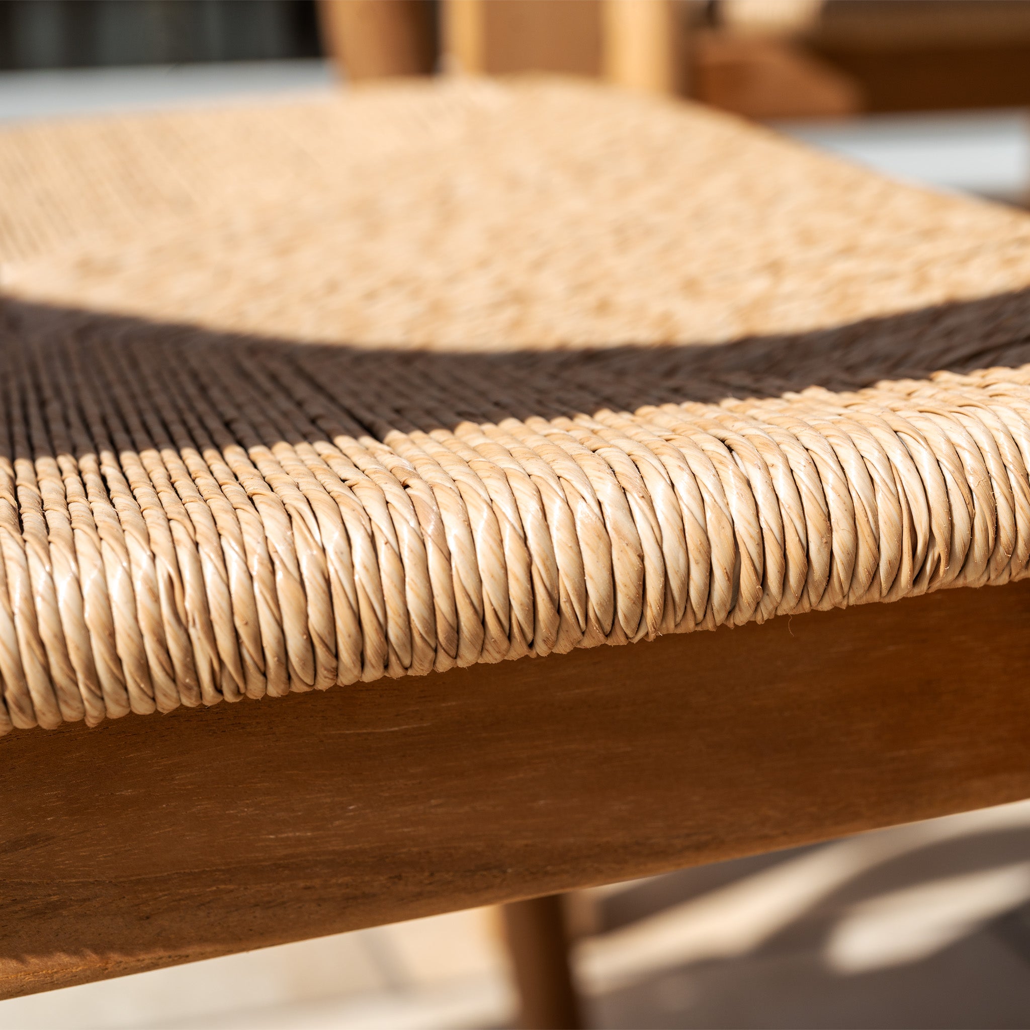 Close-up of a woven rattan seat on the Lucca 8 Seat Dining Set with Teak Table in Natural Weave, sunlight casting shadows—ideal for stylish outdoor dining.