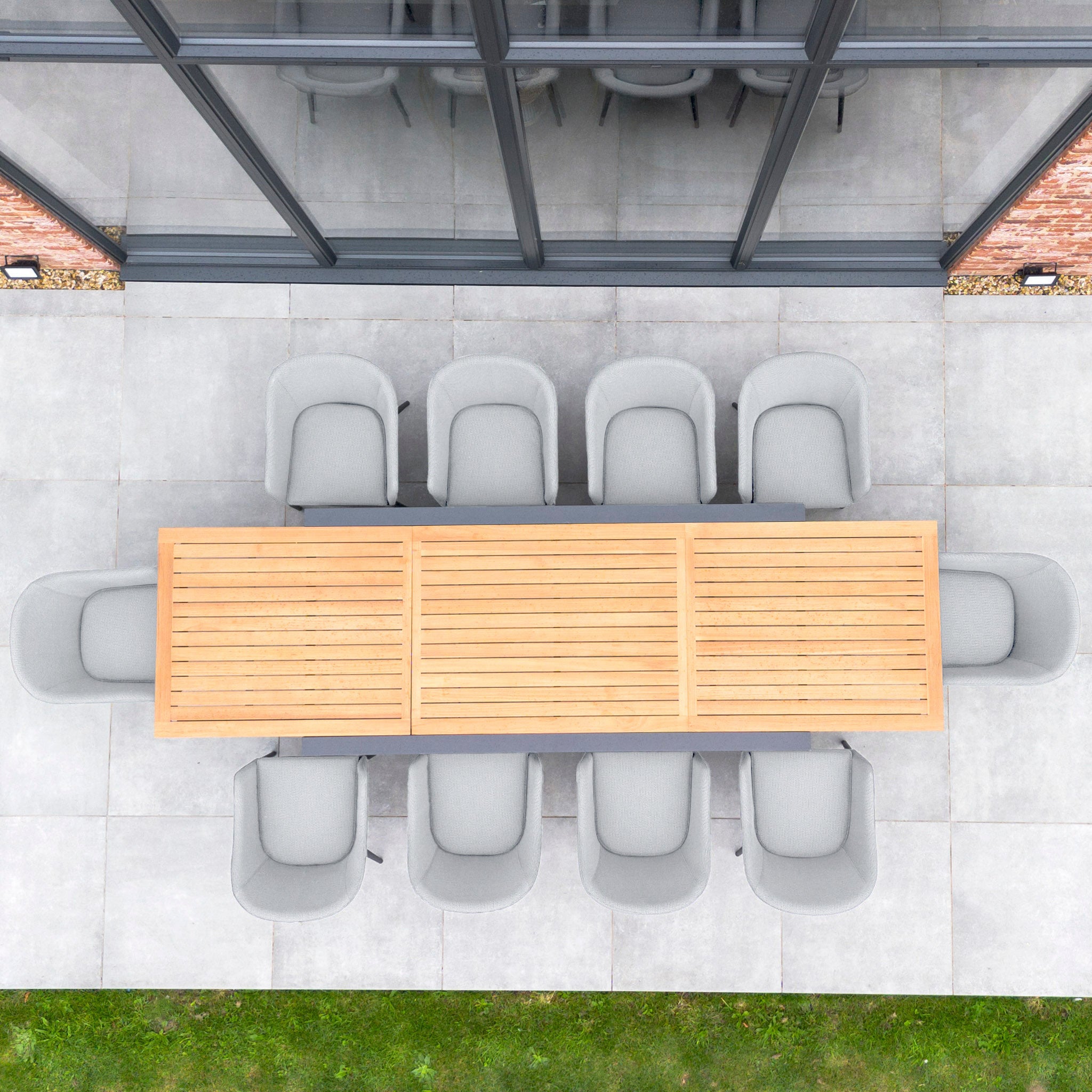 Top view of the Luna 10 Seat Outdoor Fabric Extending Teak Dining Set in Oyster Grey, featuring eight gray, stain-proof chairs on a patio near a glass wall and green grass.