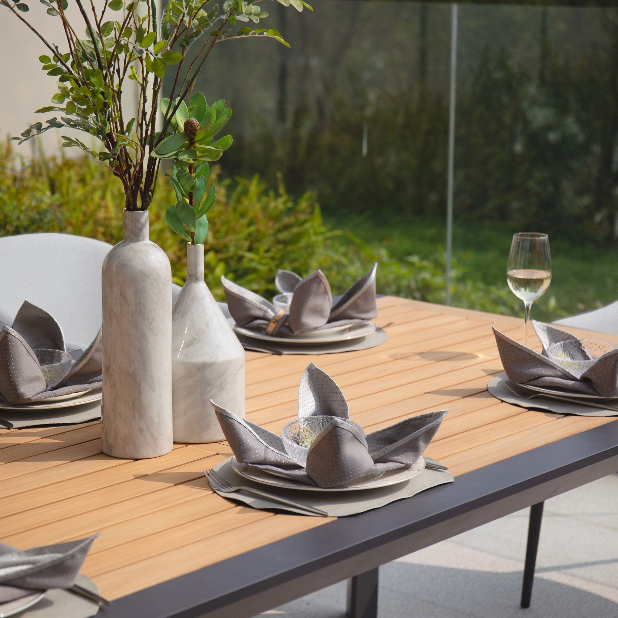 Luna 8 Seat Outdoor Fabric Extending Teak Dining Set in Oyster Grey, complete with folded napkins, decorative vases, and a glass of white wine in a garden setting. This elegant and durable extending teak dining set features maintenance-free outdoor fabric, perfect for all your alfresco gatherings.