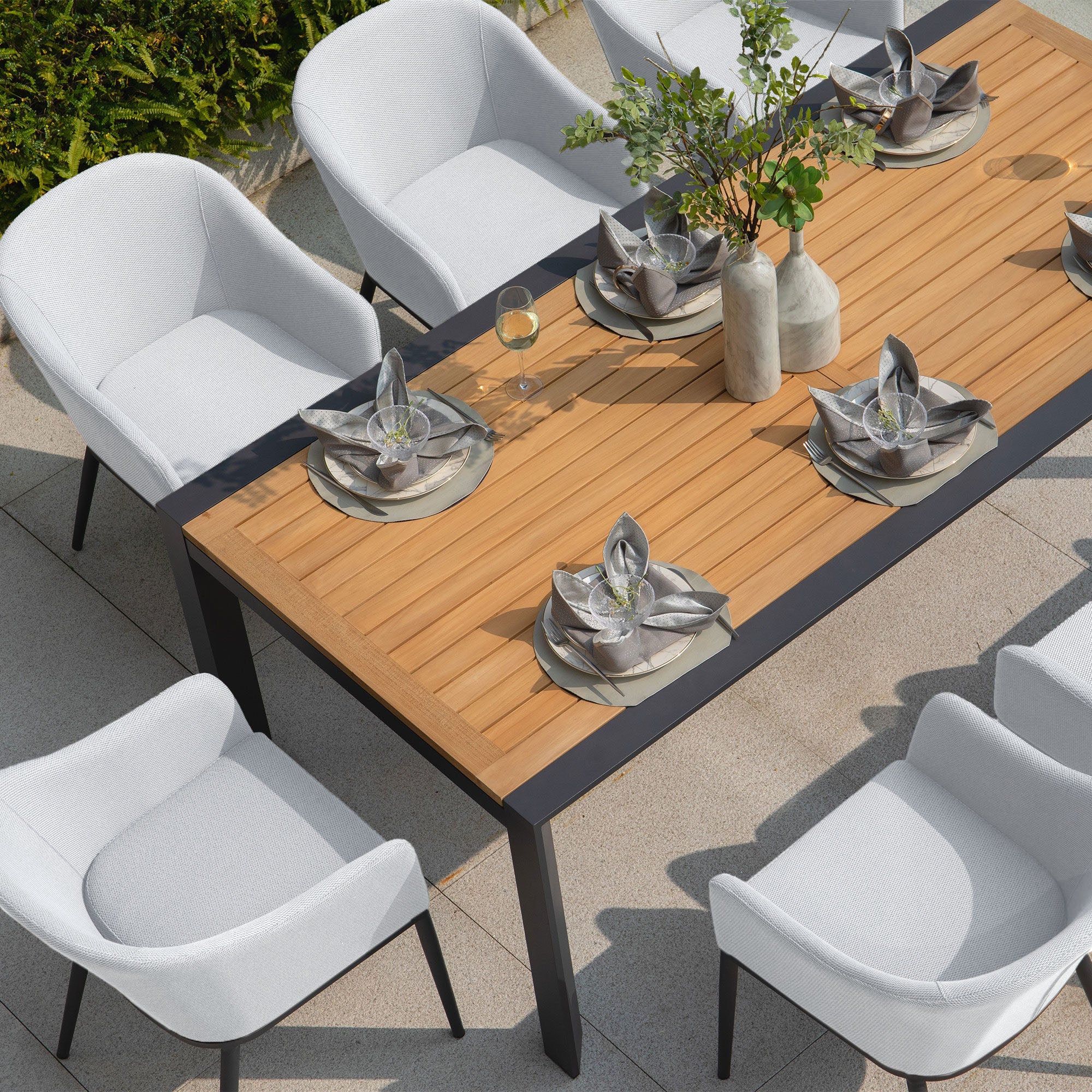 The Luna 8 Seat Outdoor Fabric Extending Teak Dining Set in Oyster Grey features a wooden top dining table, perfect for outdoor gatherings. It comes set with plates, napkins, and glassware, and is surrounded by white cushioned chairs crafted from durable outdoor fabric. This stylish teak dining set promises a maintenance-free experience for all your gatherings.