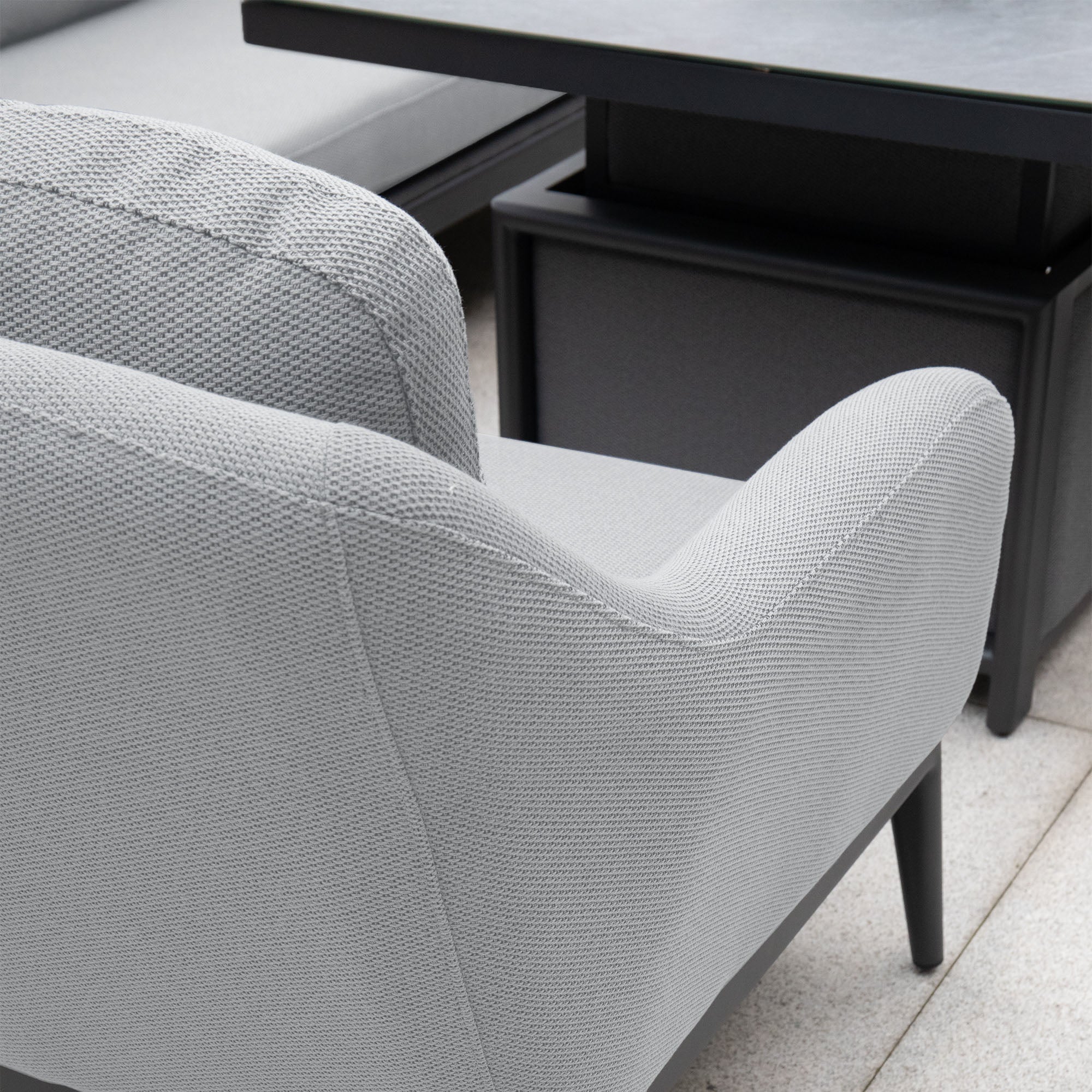 Close-up of a Luna Armchair in Oyster Grey from Harbour Lifestyle with sleek, modern design, positioned near a black square table on a tiled floor, showcasing its durable outdoor fabric.