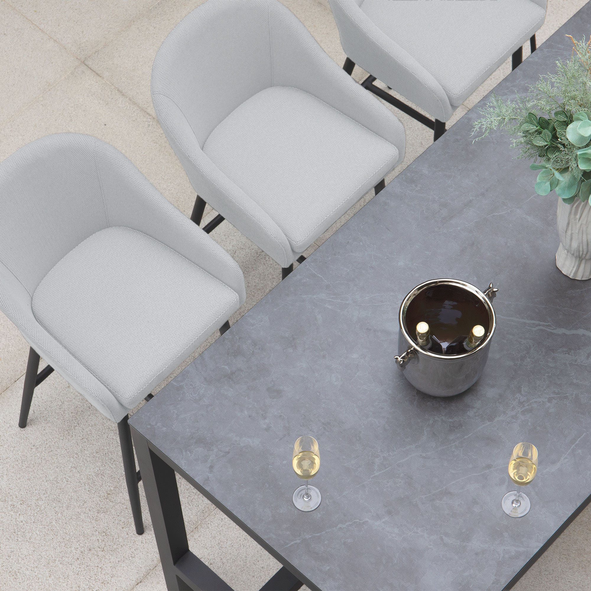 Aerial view of the Luna 8 Seat Bar Set in Oyster Grey featuring a modern dining table with a marble top, gray chairs upholstered in Luna outdoor fabric, complemented by a vase of greenery, an ice bucket, and two glasses of wine.