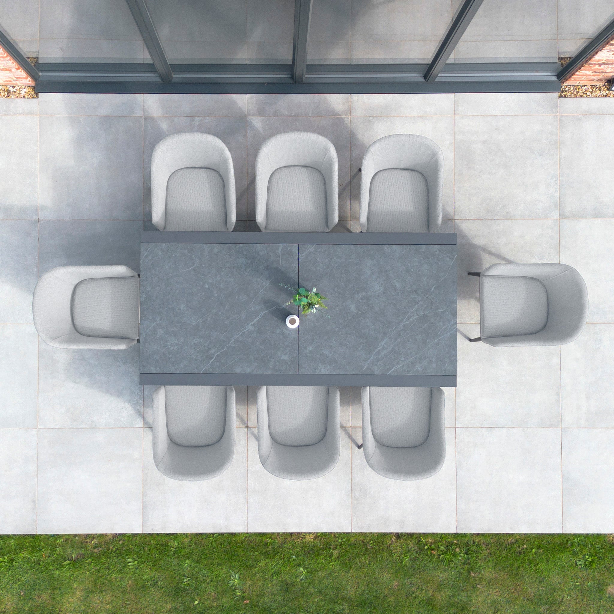 Top view of a modern outdoor dining setup featuring the Luna 8 Seat Outdoor Fabric Extending Ceramic Dining Set in Oyster Grey, complete with a rectangular table, eight chairs upholstered in Luna outdoor fabric, and a small plant centerpiece.