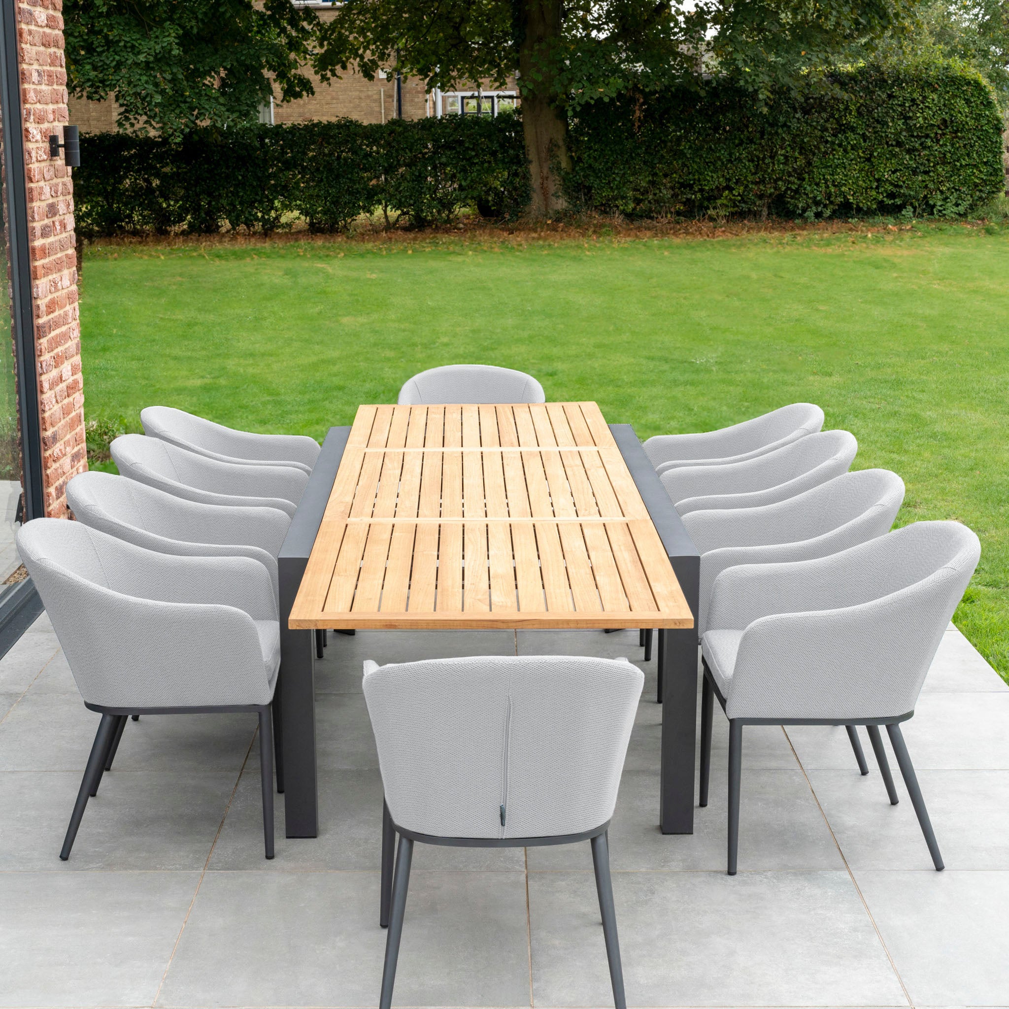 Outdoor patio with the Luna 10 Seat Outdoor Fabric Extending Teak Dining Set in Oyster Grey, surrounded by greenery.