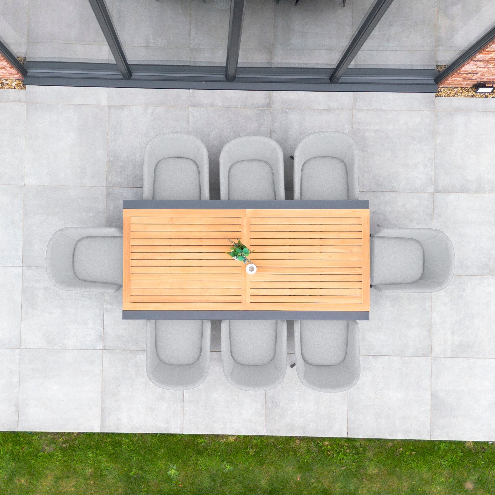 Top view of the Luna 8 Seat Outdoor Fabric Extending Teak Dining Set in Oyster Grey, featuring eight gray chairs, situated on a patio adjacent to a glass wall.