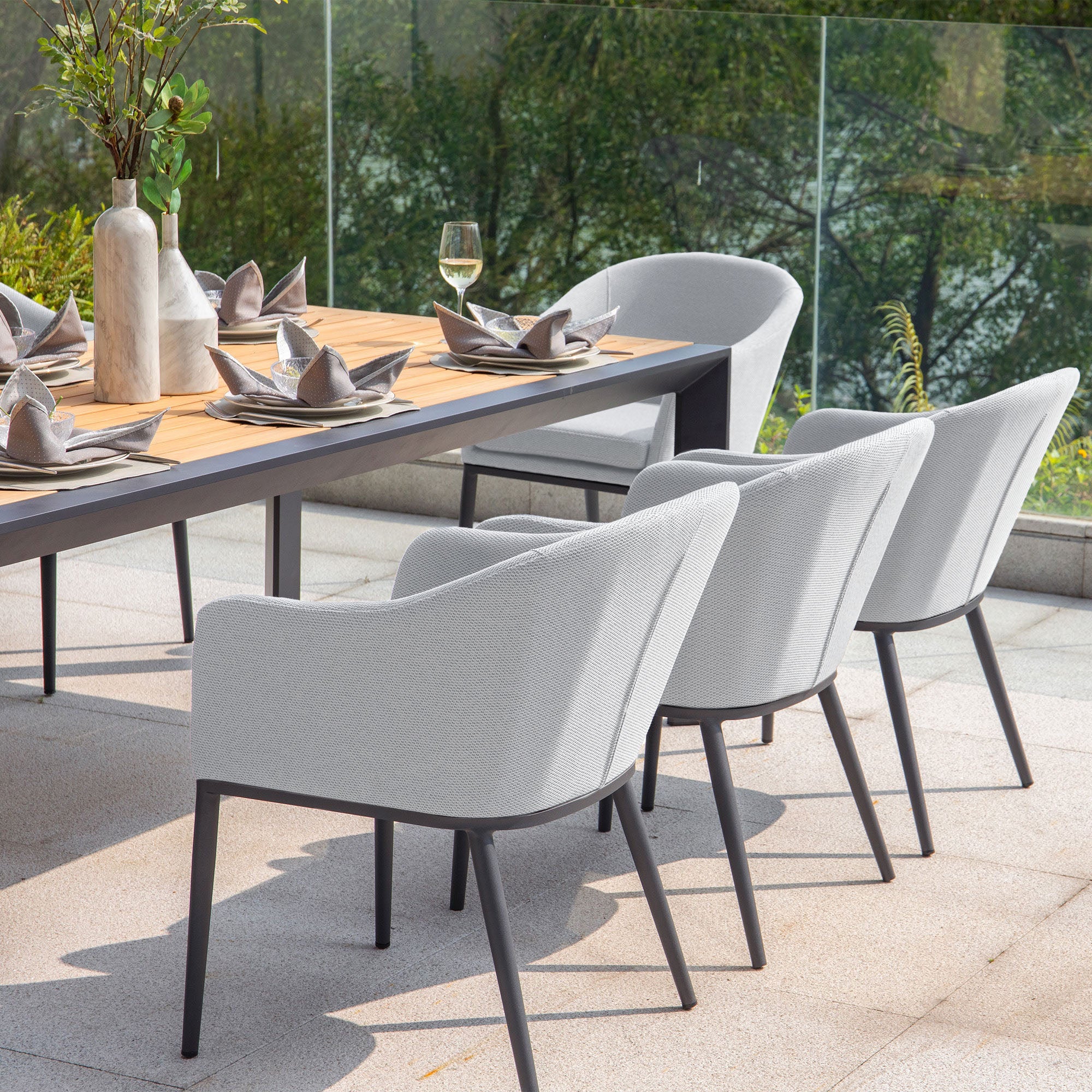 Modern outdoor dining setup featuring the Luna 8 Seat Outdoor Fabric Extending Teak Dining Set in Oyster Grey with six grey chairs made from durable outdoor fabric, arranged around a wooden table set with plates, glasses, and napkins.