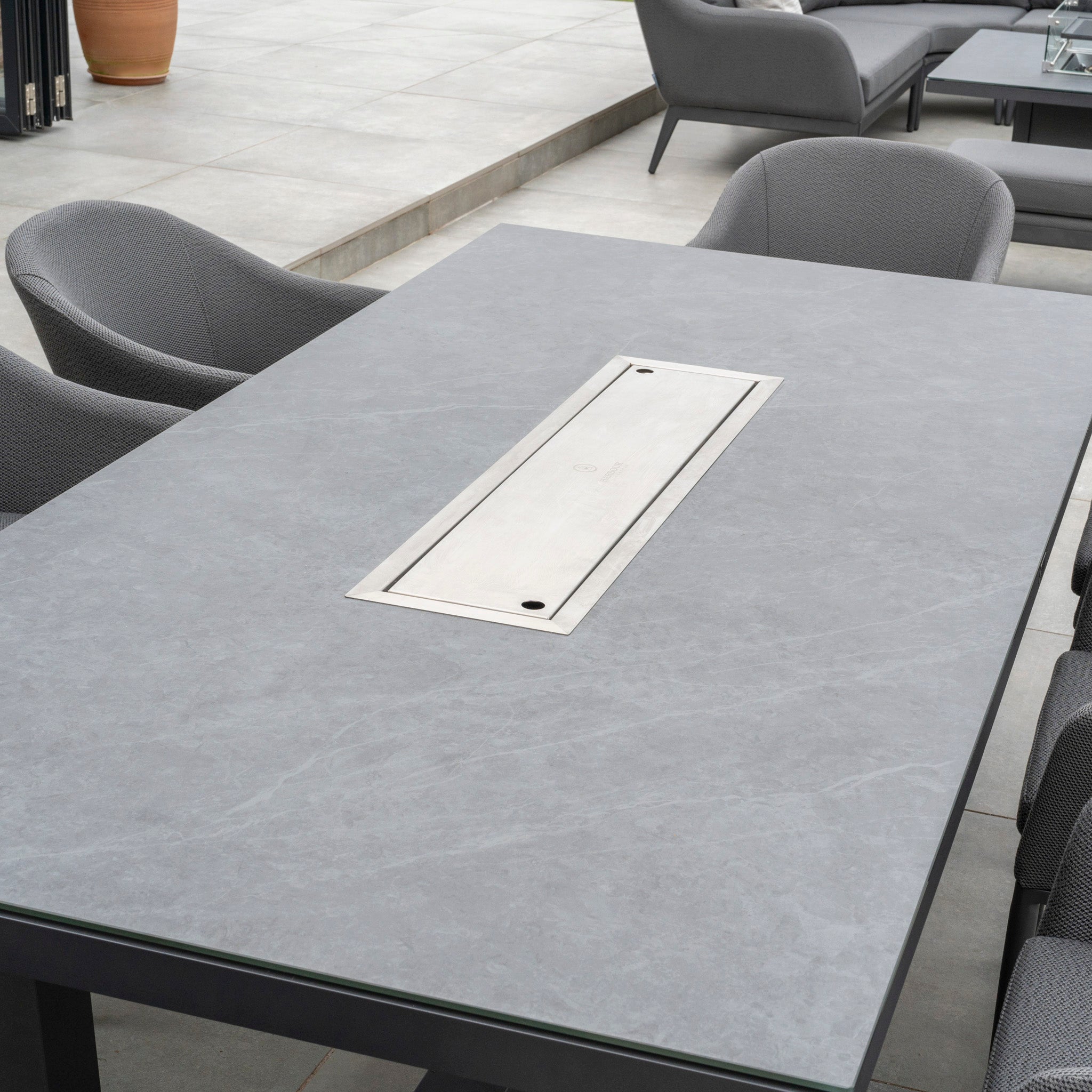 The Luna 8 Seat Outdoor Fabric Rectangular Ceramic Firepit Dining Set in Grey features a modern outdoor dining table with a sleek grey surface and is surrounded by grey upholstered chairs crafted from durable Luna outdoor fabric, making it perfect for any patio.