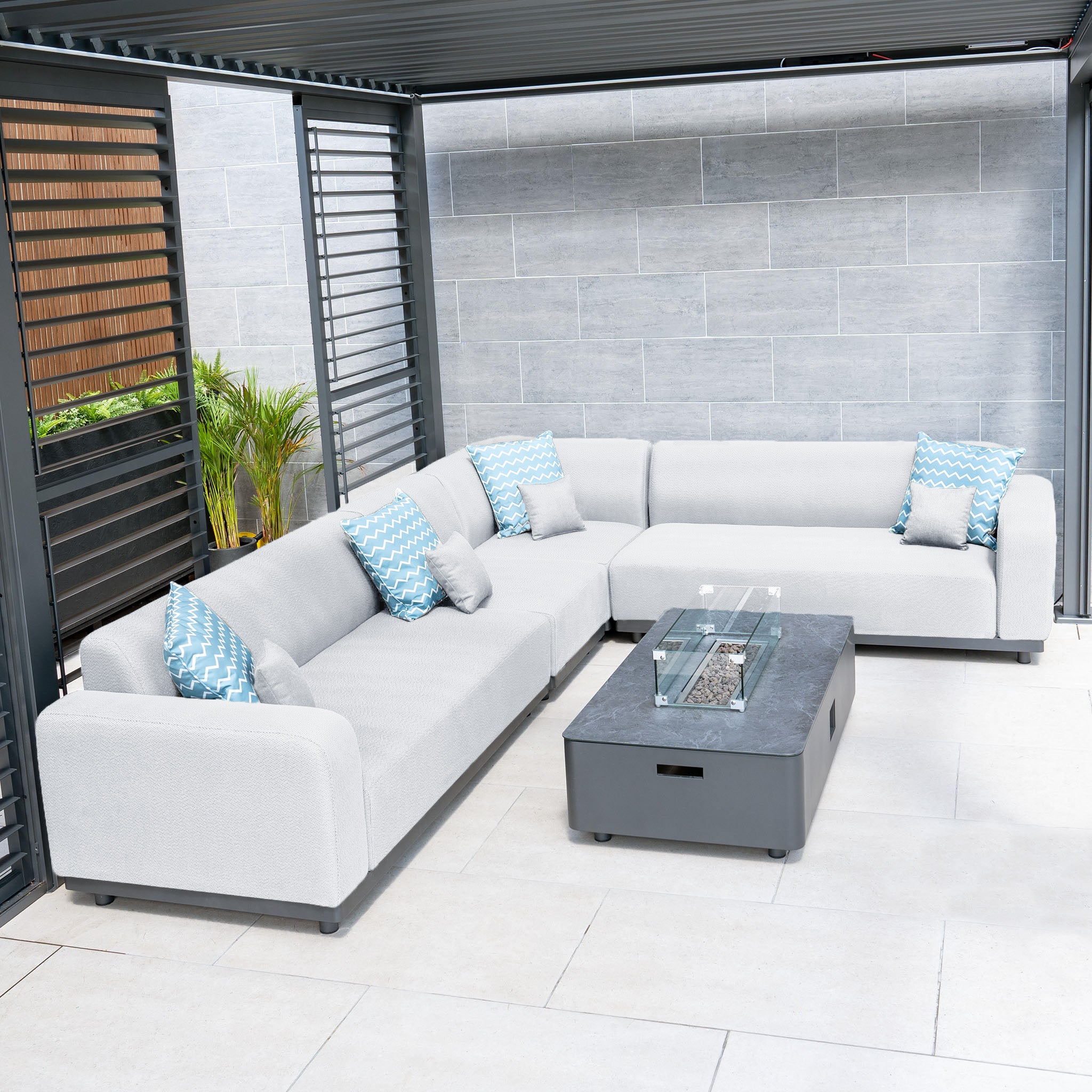 Outdoor patio featuring the Luna Outdoor Fabric Large Corner Group Set in Oyster Grey with a modern firepit coffee table and blue patterned pillows under a pergola.
