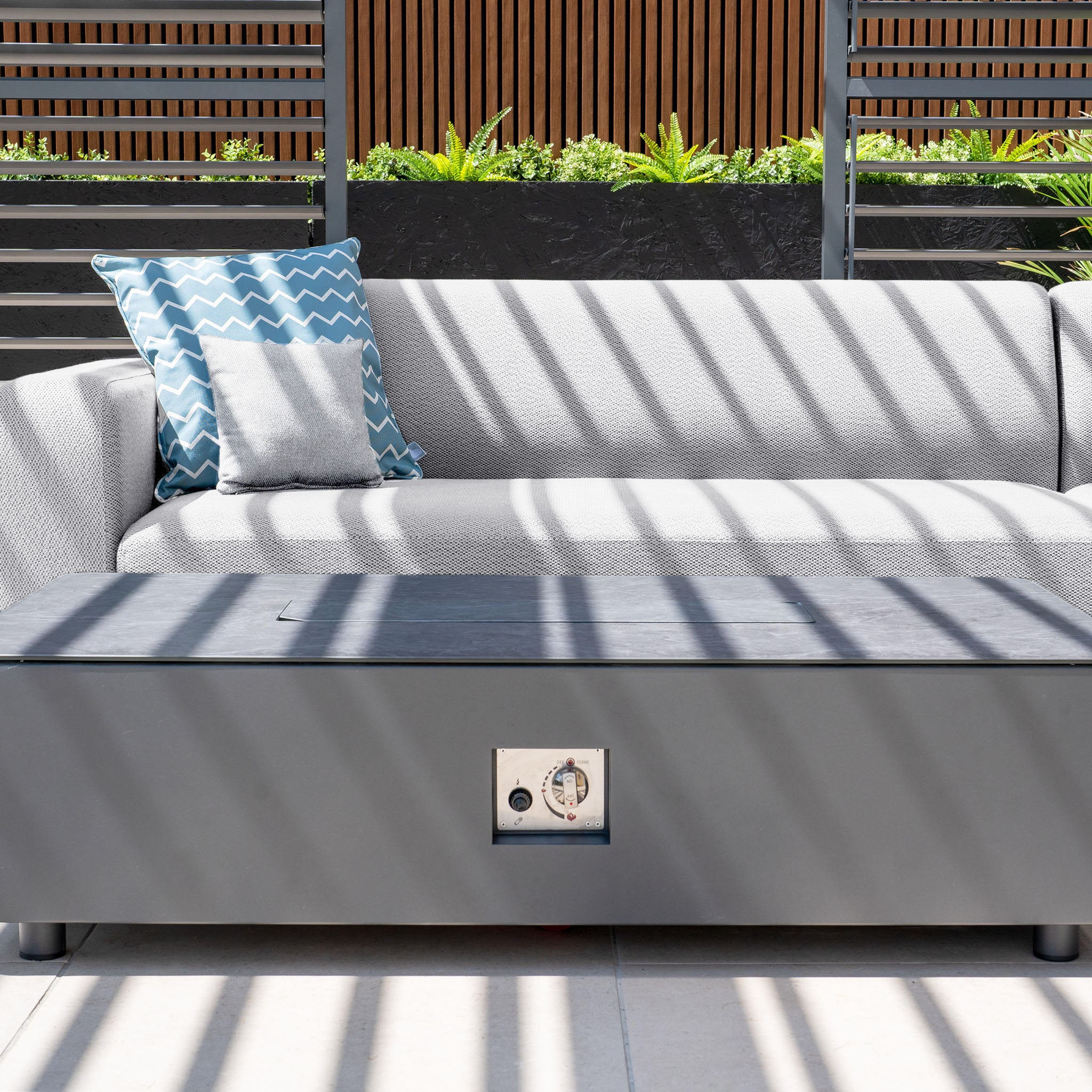 Outdoor seating area featuring the Luna Outdoor Fabric Large Corner Group Set in Oyster Grey, complete with geometric pillows, a stain-proof firepit coffee table, and wooden slat accents.
