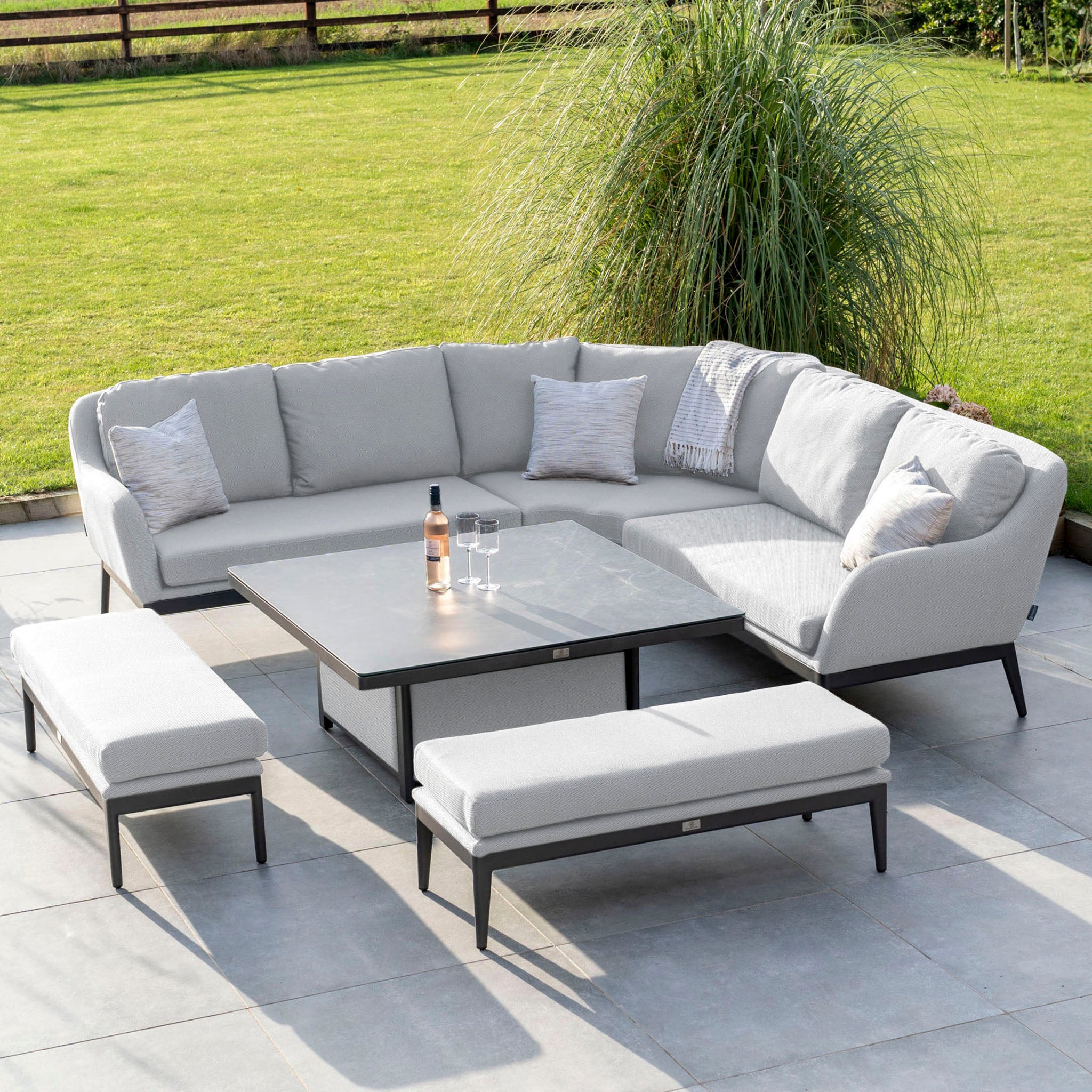 Experience outdoor relaxation with the Luna Deluxe Outdoor Fabric Square Corner Dining Set in Oyster Grey, featuring a comfortable L-shaped sofa, cushioned benches, and a versatile rising rectangular table on a tiled floor.