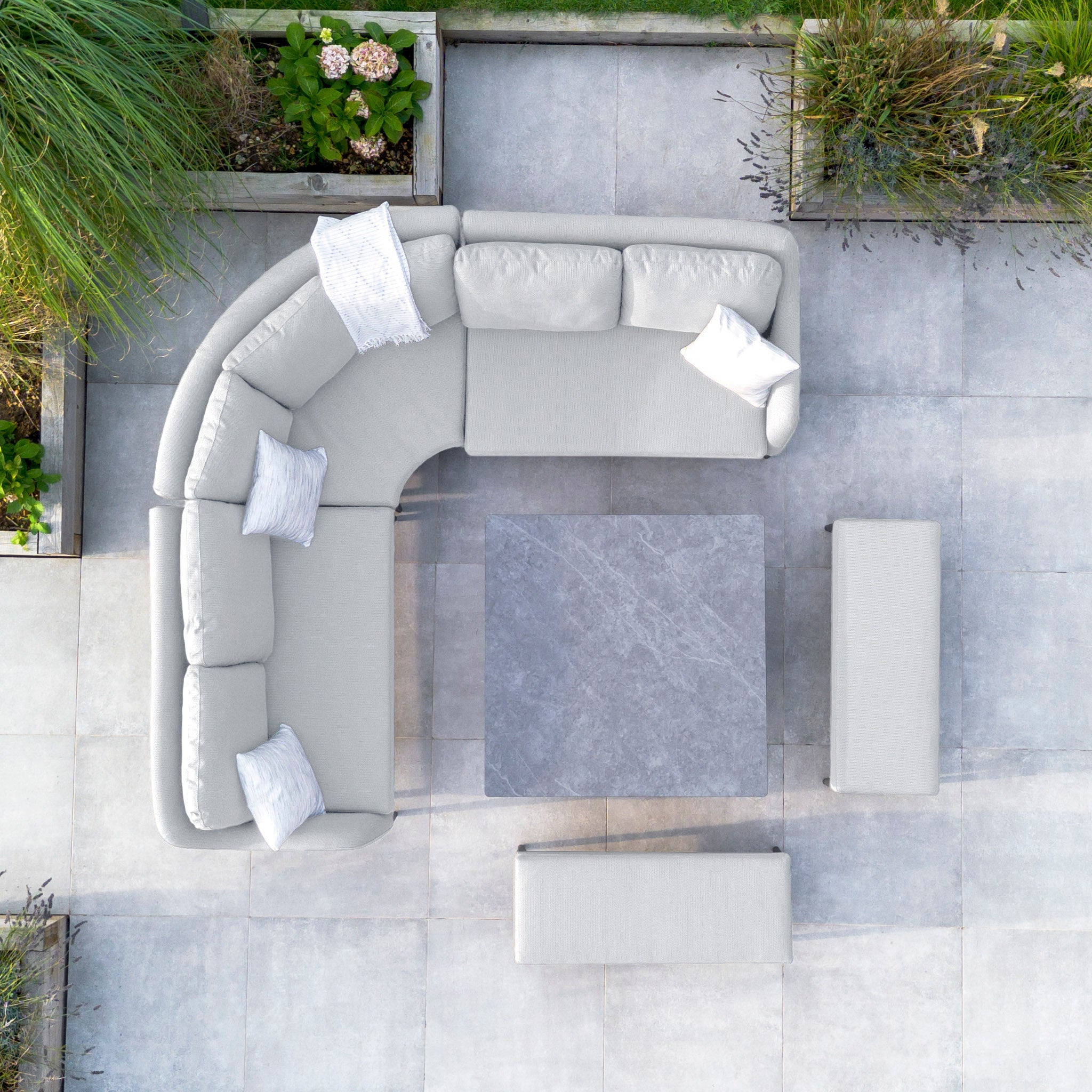 Top view of a modern outdoor seating area showcasing the Luna Deluxe Outdoor Fabric Square Corner Dining Set with Rising Table in Oyster Grey, complete with cushions and an adjustable stone table on a tiled patio.