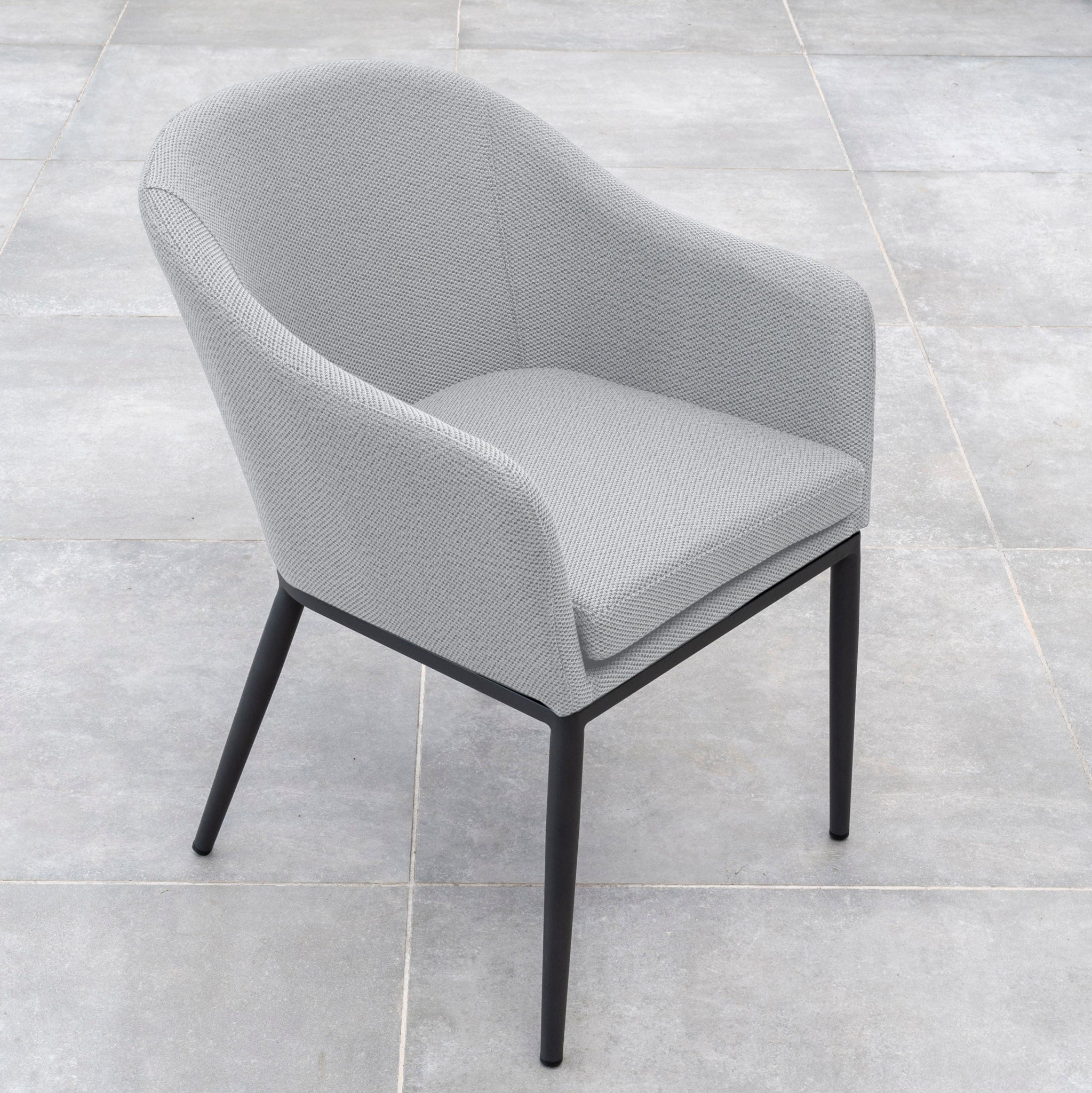 A modern, light gray upholstered chair with black legs set on a tiled floor, perfect for complementing your Luna 8 Seat Outdoor Fabric Extending Teak Dining Set in Oyster Grey.