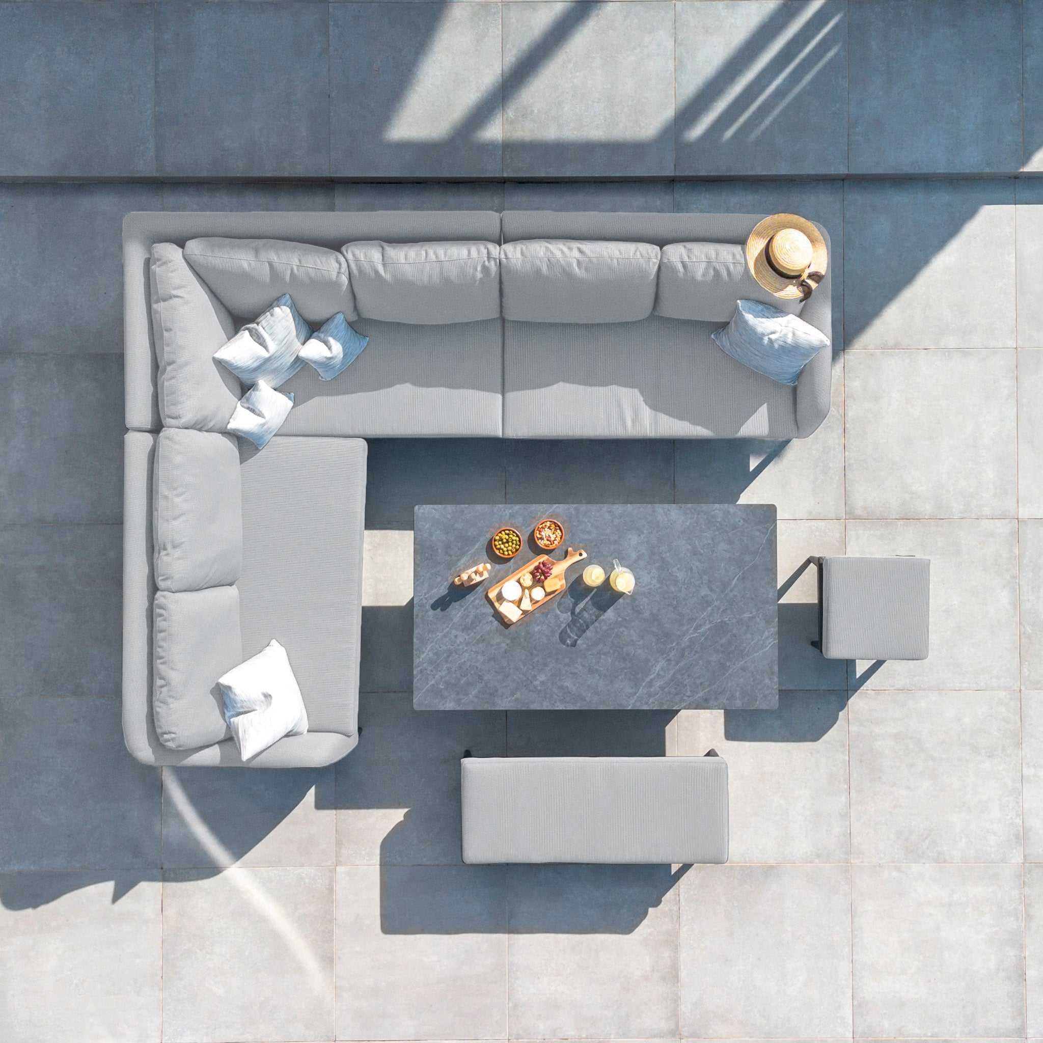 Top-down view of the Luna Outdoor Fabric Rectangular Corner Dining Set with Rising Table in Oyster Grey (Left Hand), featuring snacks and drinks on the table, and sunlight casting shadows.