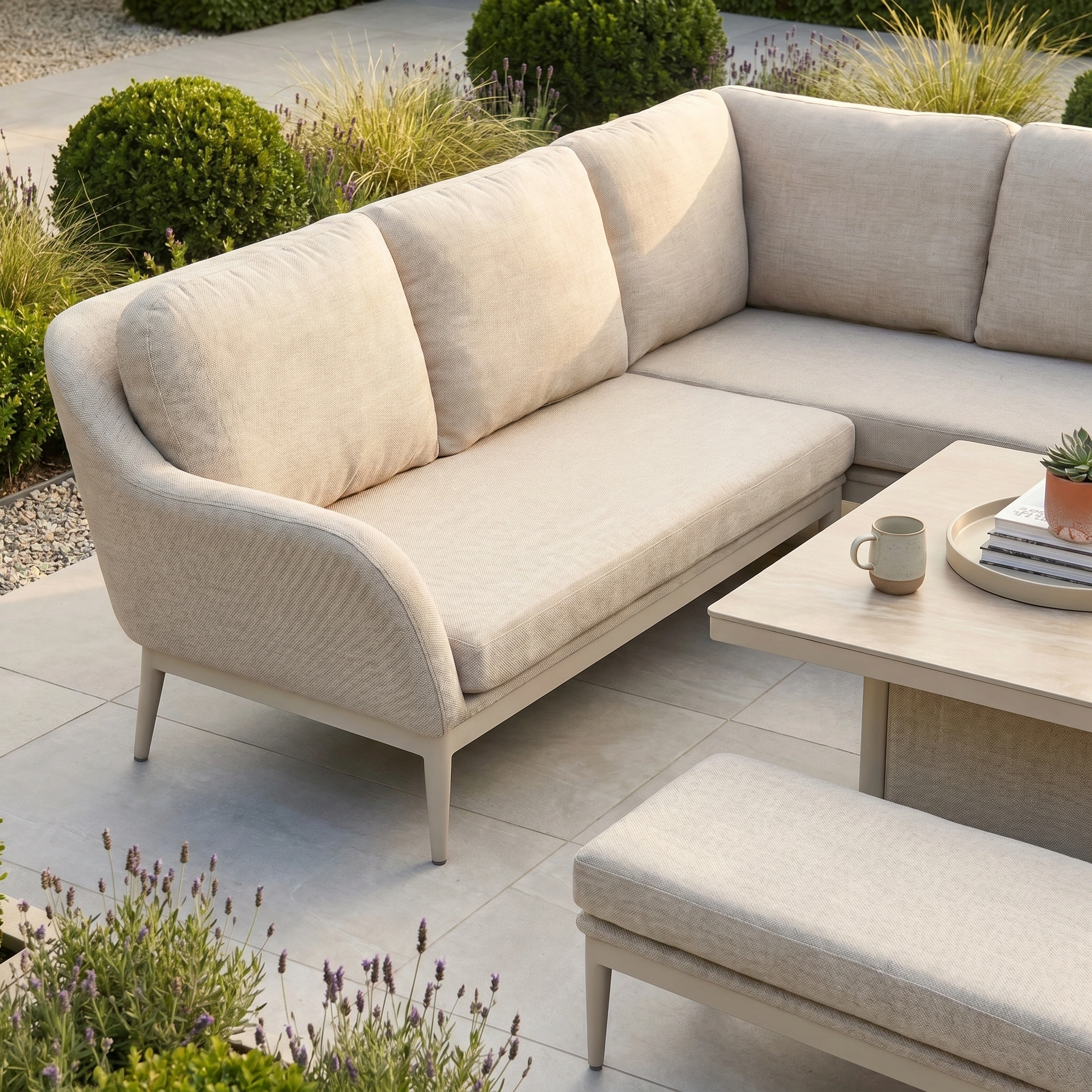 The Luna Outdoor Fabric Rectangular Corner Dining Set with Rising Table in Fawn (Left Hand) sits on a tiled patio, topped with a coffee table and mug, surrounded by greenery. Crafted from all-weather materials for lasting outdoor comfort.