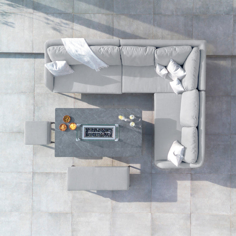 Top view of a modern outdoor patio setup featuring the Luna Outdoor Fabric Rectangular Corner Dining Set with a Rising Firepit Table in Oyster Grey (Right Hand), complemented by stools and decorative items.