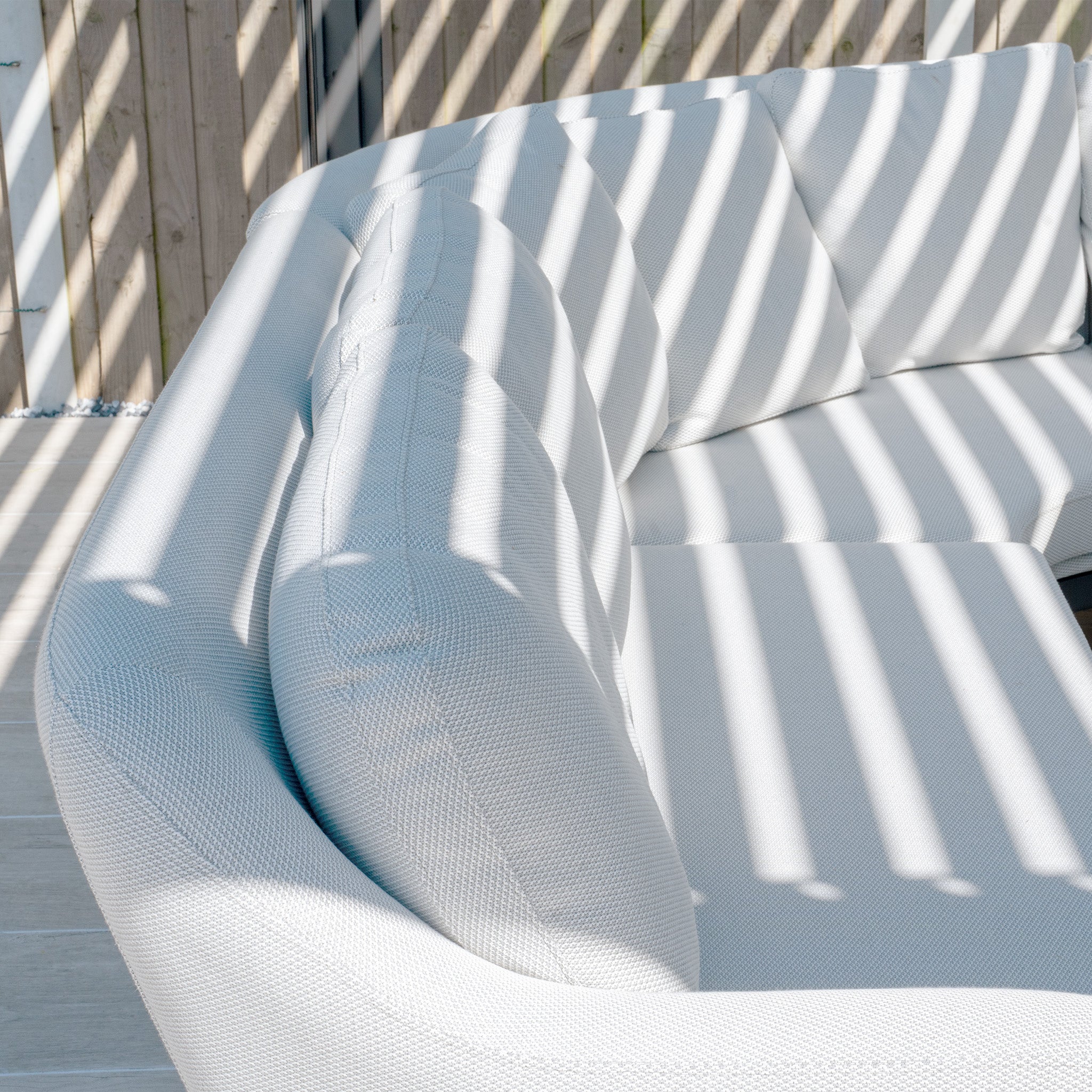 Curved white Harbour Lifestyle Monterrey 3 Seat Sofa Set with sunlight creating striped shadows through vertical blinds, featuring reflex foam cushions and a hydrophobic thin rope weave, now available as Ali testing vimeo - no video.