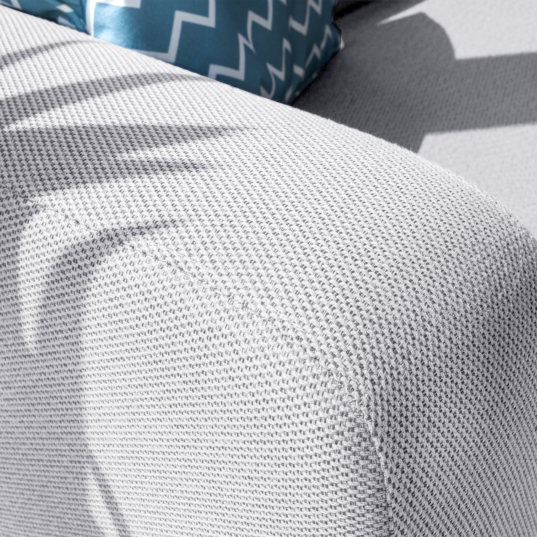 Close-up of the Luna Outdoor Fabric Large Corner Group Set in Oyster Grey, showcasing a textured sofa and a blue and white zigzag pillow. The included firepit coffee table adds coziness, while the stain-proof material ensures durability and easy maintenance.
