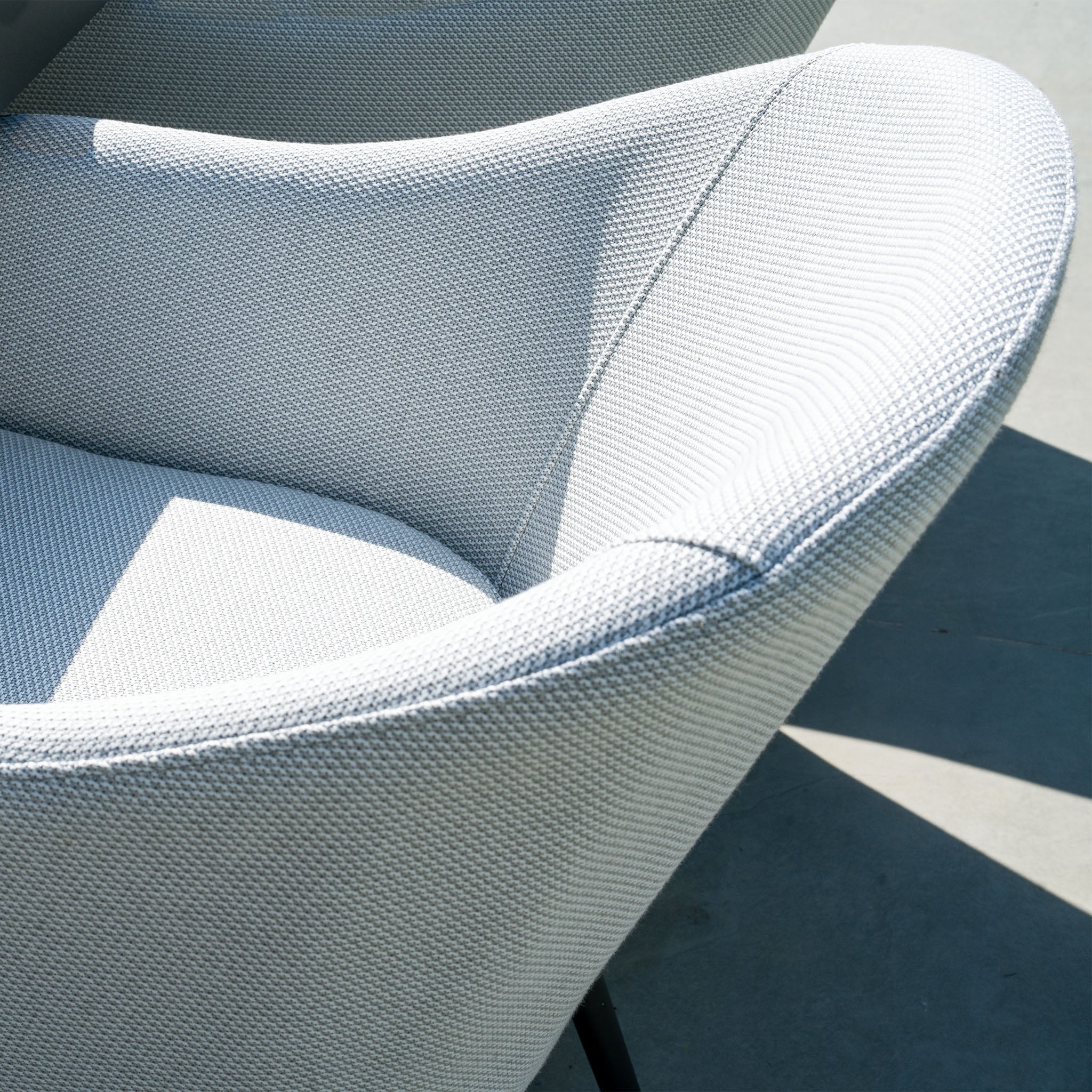 Close-up of a modern, light-gray upholstered Luna 8 Seat Outdoor Fabric Rectangular Ceramic Firepit Dining Set in Oyster Grey, featuring curved armrests, basking in sunlight.