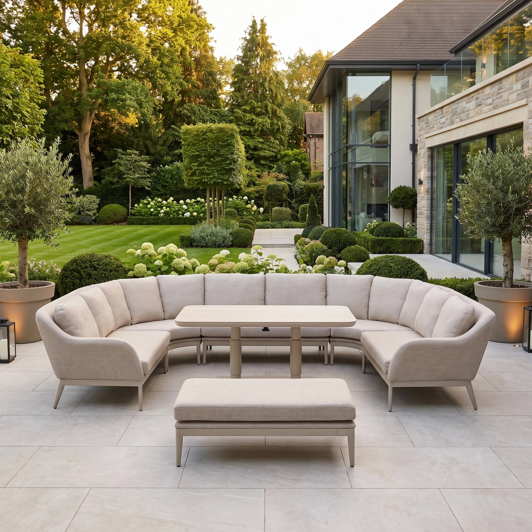 The Luna U-Shape Outdoor Fabric Corner Dining Set with Altura Rising Table in Fawn features a contemporary curved design with a spacious corner layout and matching bench, showcased on a patio overlooking a landscaped garden.