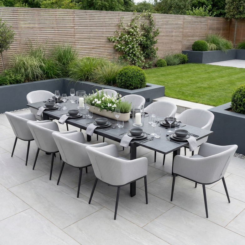 The Luna 10 Seat Outdoor Fabric Extending Ceramic Dining Set in Oyster Grey is perfect for patios, offering modern all-weather comfort surrounded by lush garden landscaping.