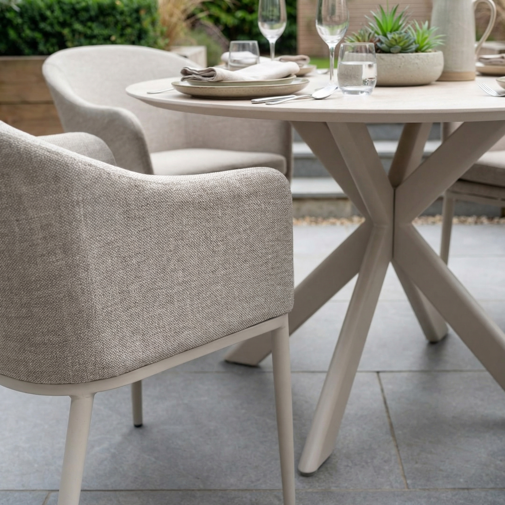 The Luna 4 Seat Round Outdoor Fabric Dining Set with Albatross Table in Fawn is arranged for outdoor dining, featuring comfortable chairs and a stylish round table—ideal for meals on a stone patio.