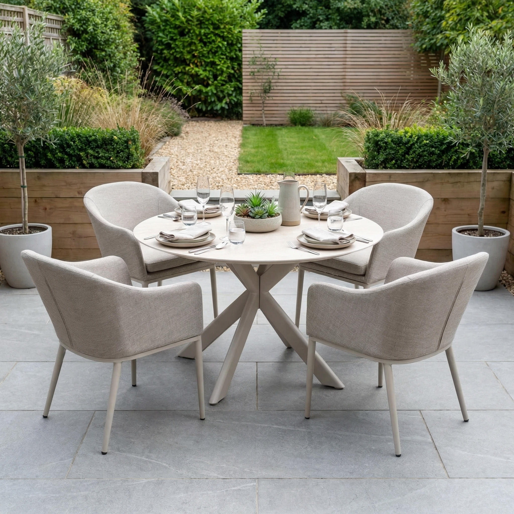 The Luna 4 Seat Round Outdoor Fabric Dining Set with Albatross Table in Fawn is stylishly arranged for dining in a modern garden, featuring four beige chairs and a round table designed for all-weather use.