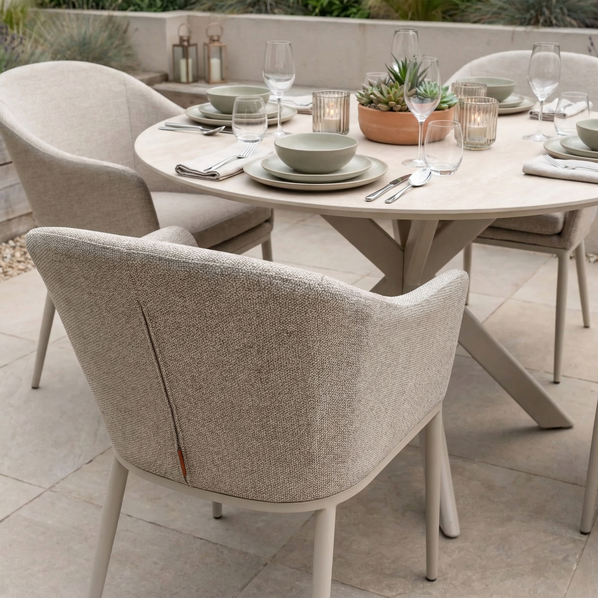 The Luna 4 Seat Round Outdoor Fabric Dining Set with Albatross Table in Fawn features cushioned all-weather chairs and a ceramic round table, perfect for outdoor dining with plates, glasses, and candles on your patio.
