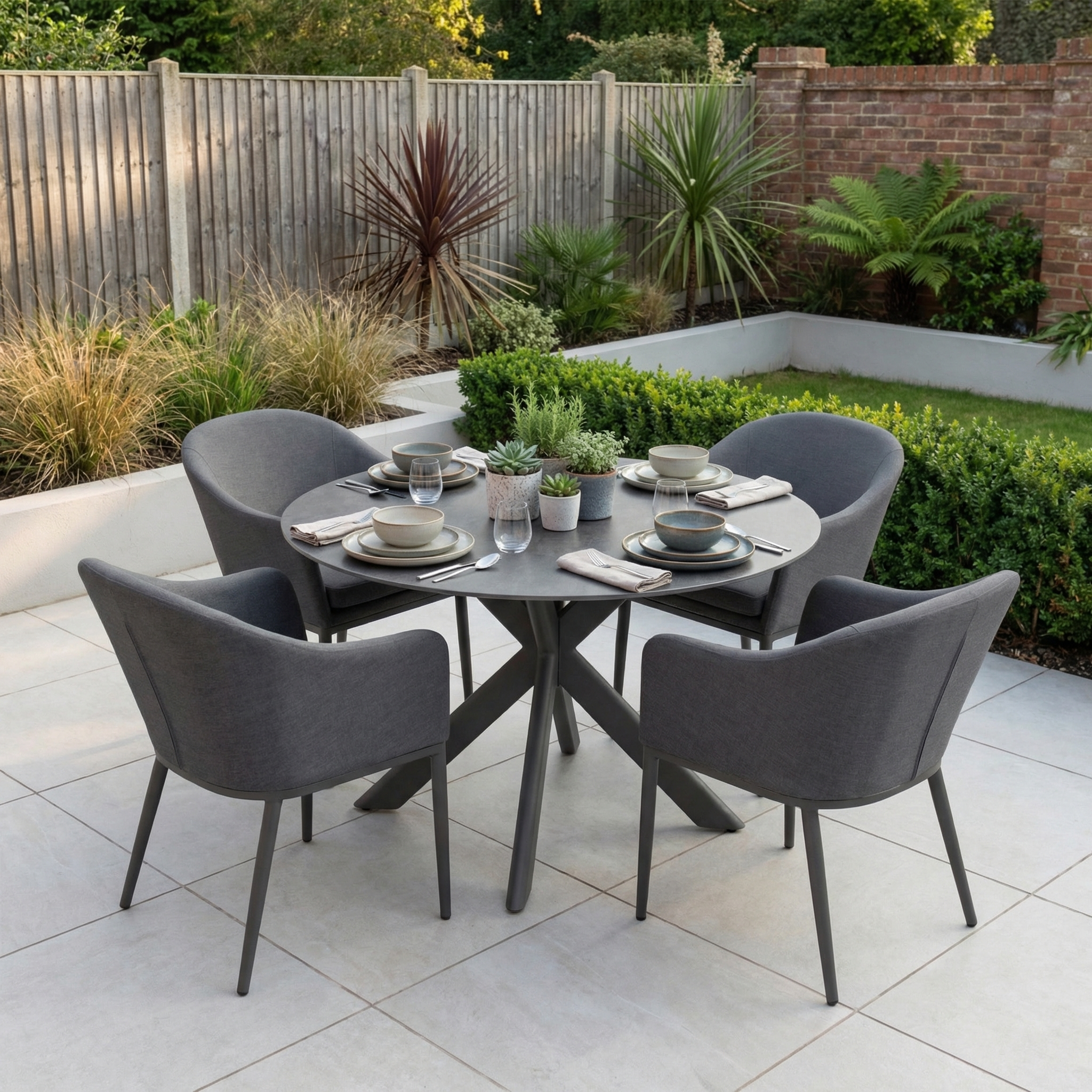 The Luna 4 Seat Round Outdoor Fabric Dining Set with Albatross Table in Grey features four grey chairs and is perfect for alfresco dining in a landscaped garden.