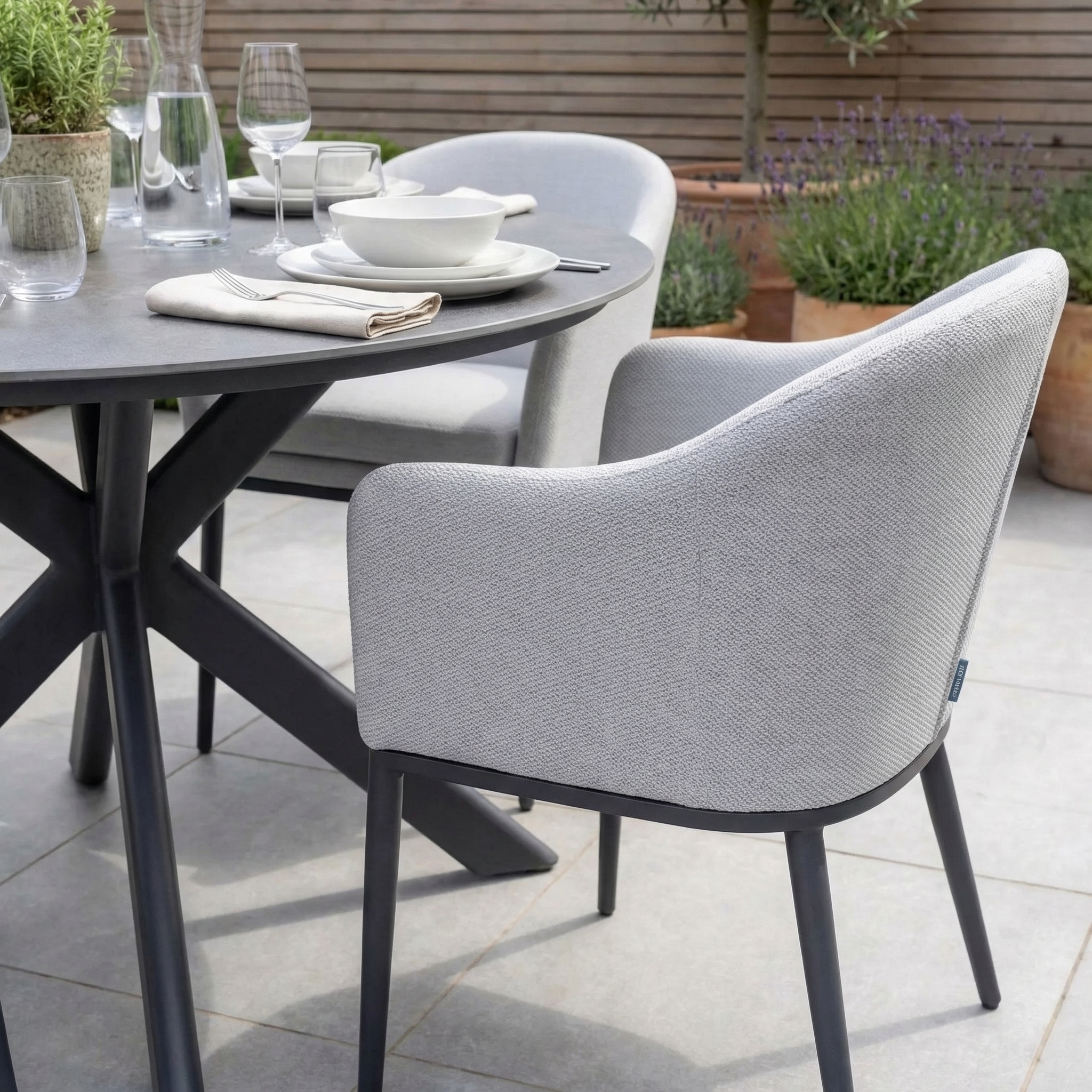 The Luna 4 Seat Round Outdoor Fabric Dining Set with Albatross Table in Oyster Grey, set with plates, glasses, and napkins on a tiled patio—perfect for stylish al fresco dining.
