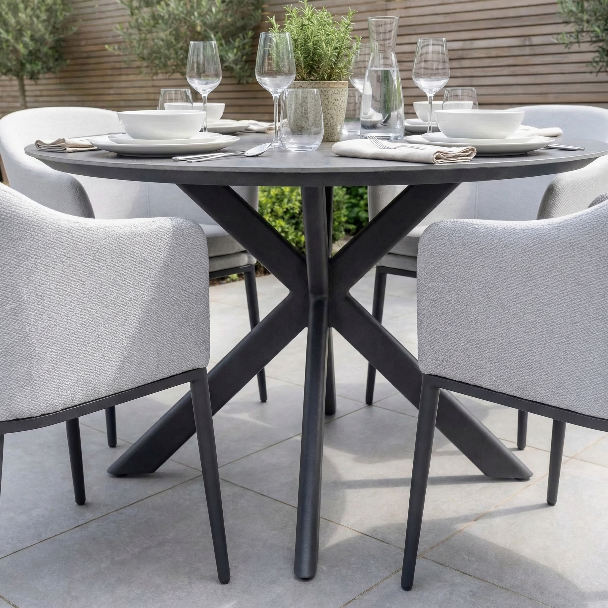 Luna 4 Seat Round Outdoor Fabric Dining Set with Albatross Table in Oyster Grey, arranged for al fresco dining with plates, glasses, and a potted plant centerpiece.