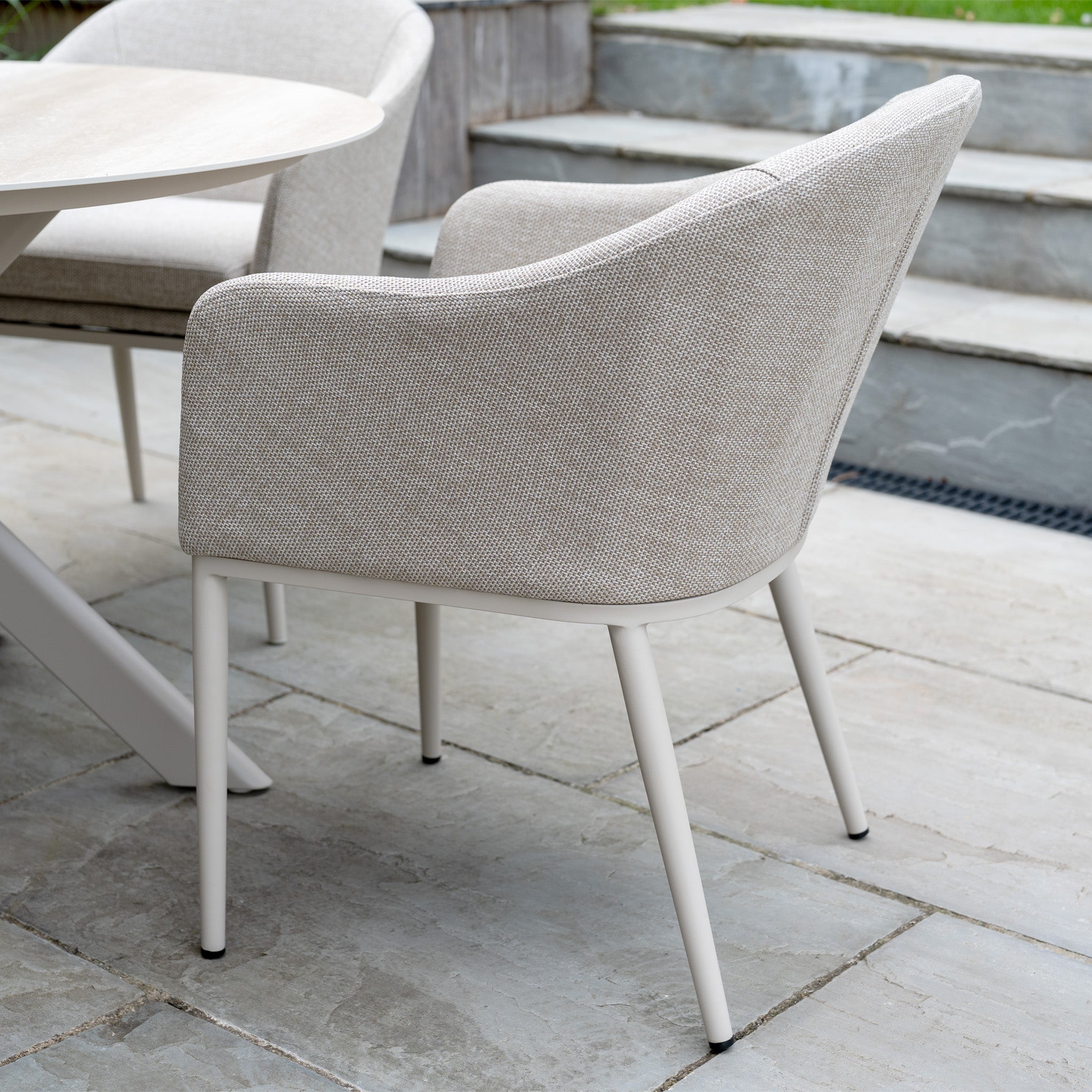 The Luna 4 Seat Round Outdoor Fabric Dining Set with Albatross Table in Fawn offers a stylish all-weather seating option, featuring beige upholstery and a round ceramic table for your stone patio.