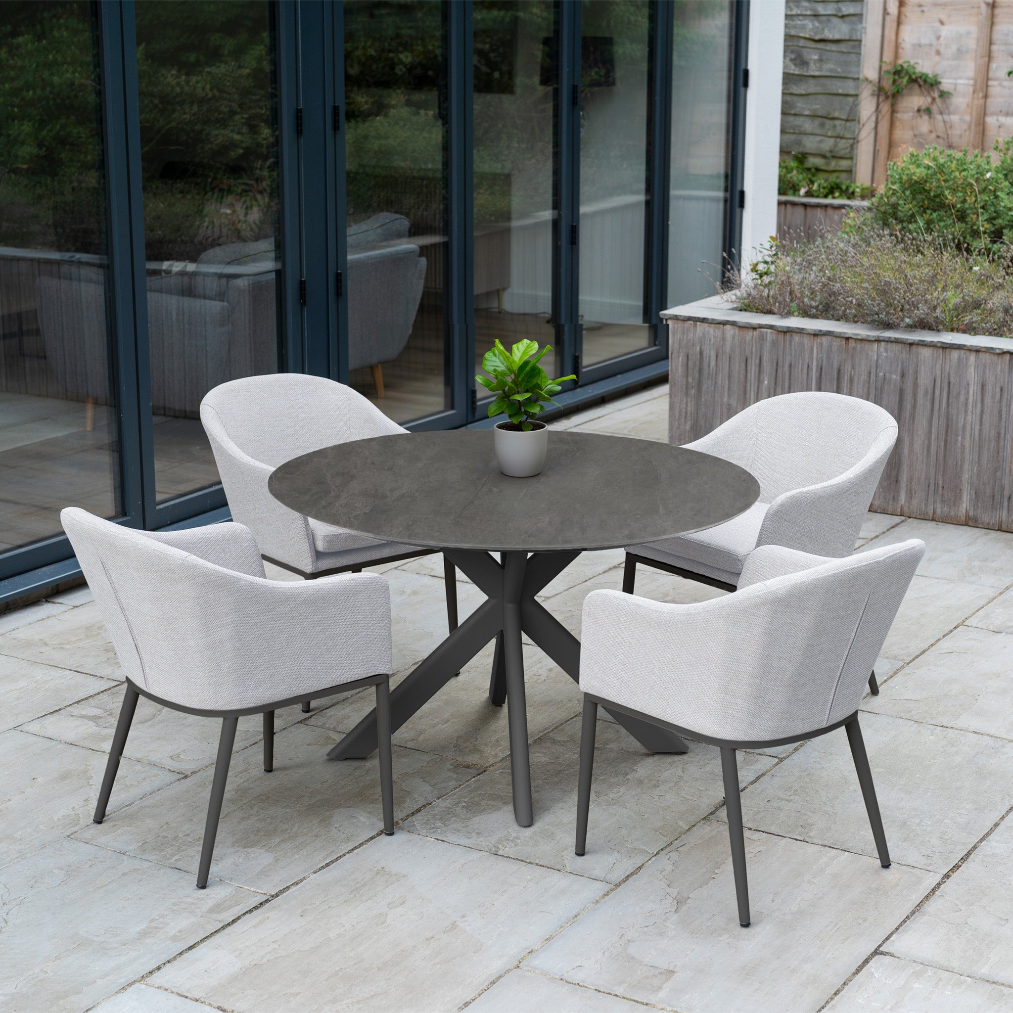 The Luna 4 Seat Round Outdoor Fabric Dining Set with Albatross Table in Oyster Grey is ideal for al fresco patio dining outside glass doors, especially when paired with a potted plant.