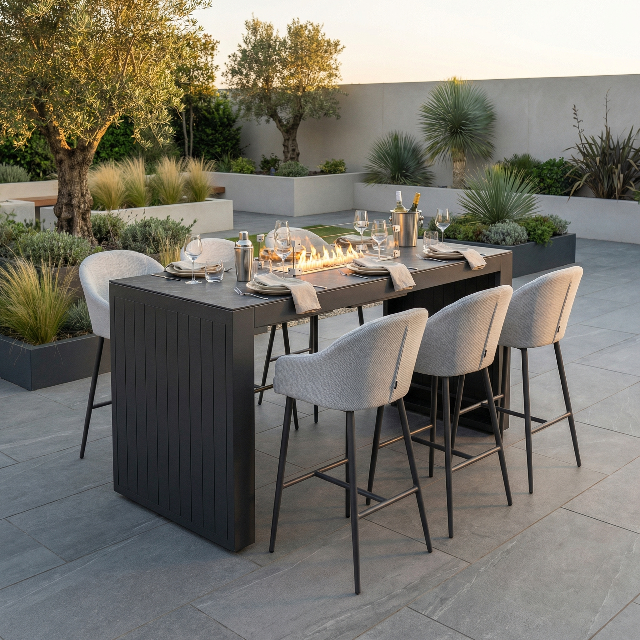 Modern outdoor dining area featuring the Luna 6 Seat Outdoor Fabric Ceramic Firepit Bar Set in Oyster Grey, complete with place settings and surrounded by lush plants.