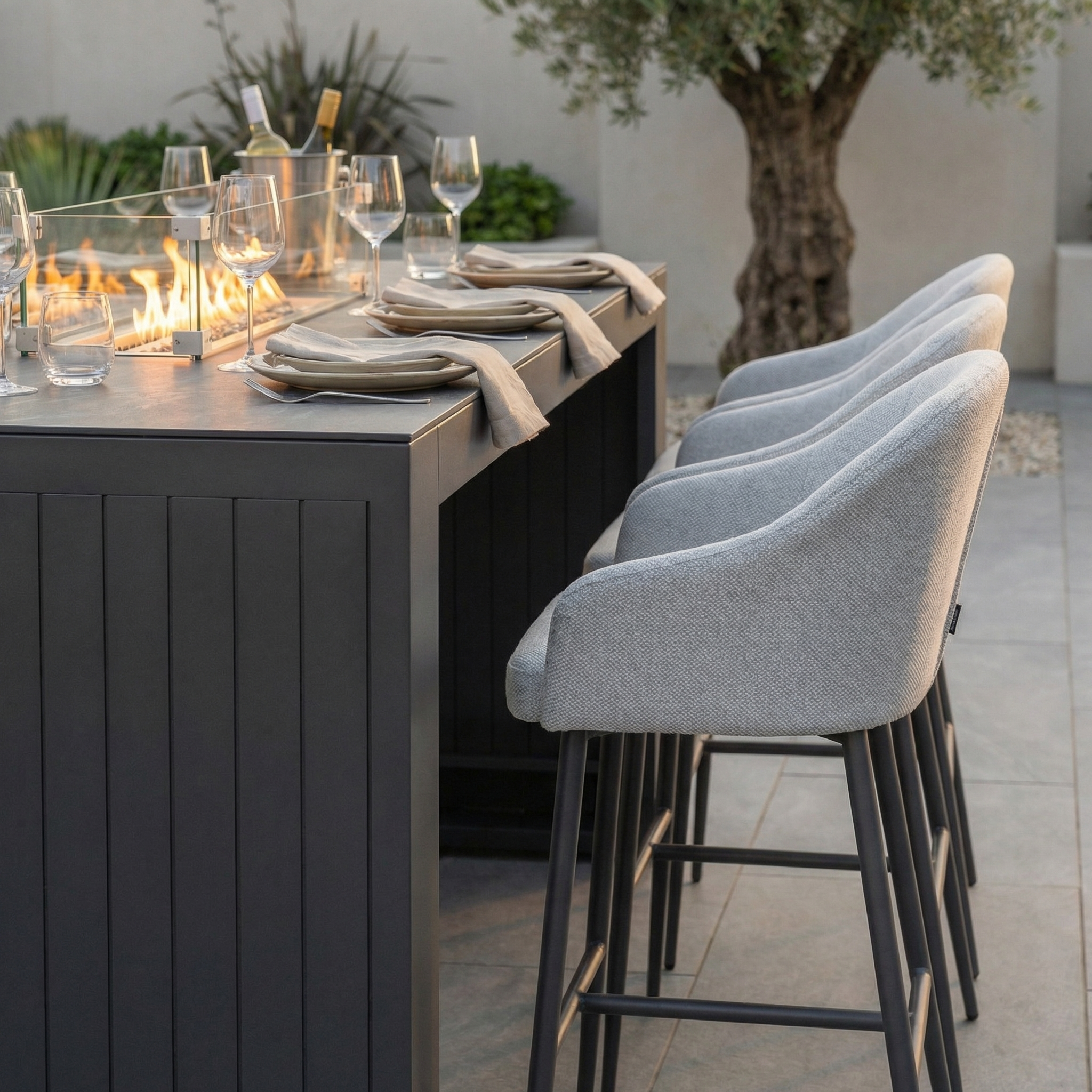 Contemporary outdoor dining area featuring the Luna 6 Seat Outdoor Fabric Ceramic Firepit Bar Set in Oyster Grey, complete with barstools and a built-in all-weather ceramic fire pit centerpiece.