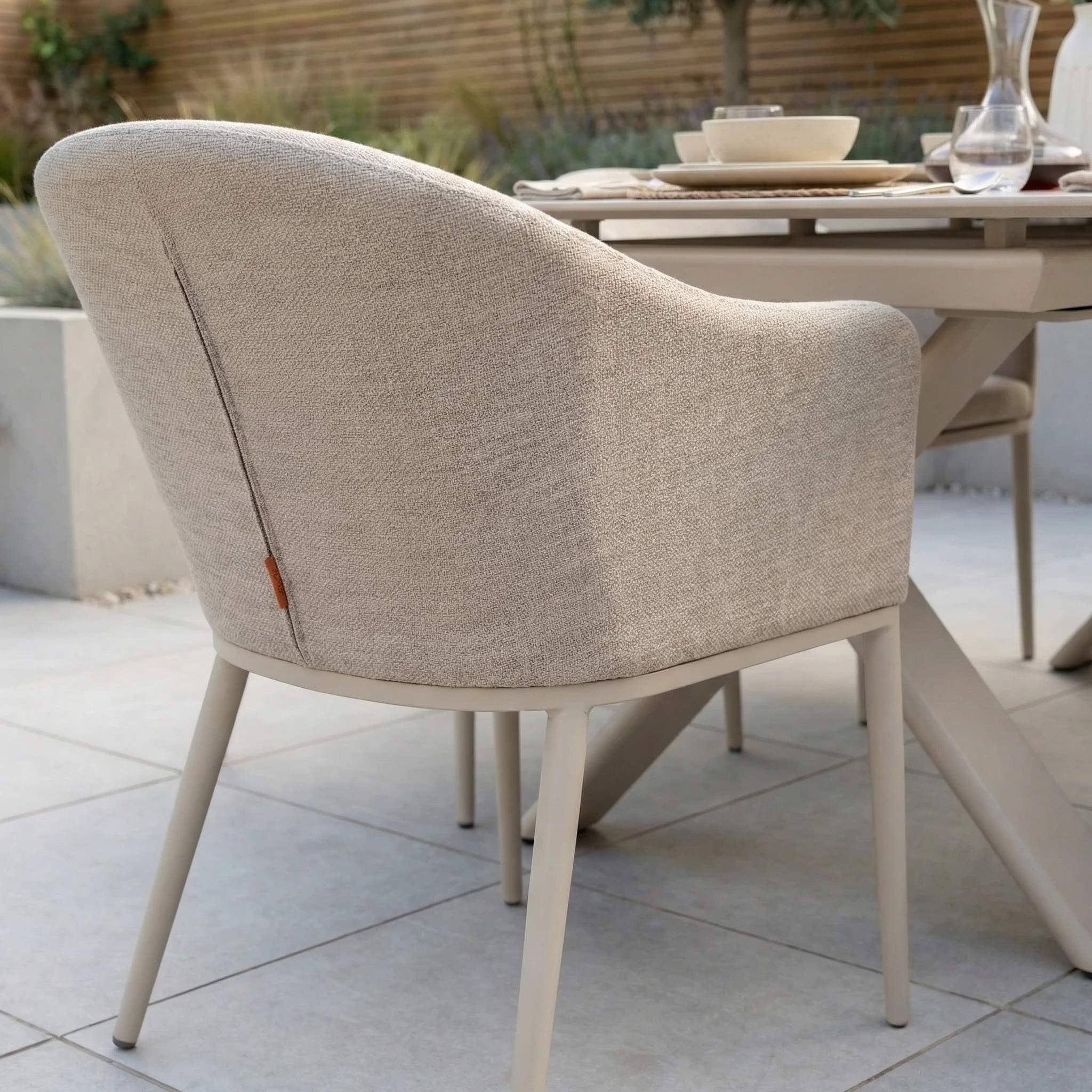 The Luna 6 Seat Outdoor Fabric Dining Set with Albatross Extending Table in Fawn sits stylishly on a tiled patio, featuring modern beige all-weather dining chairs around the outdoor table.