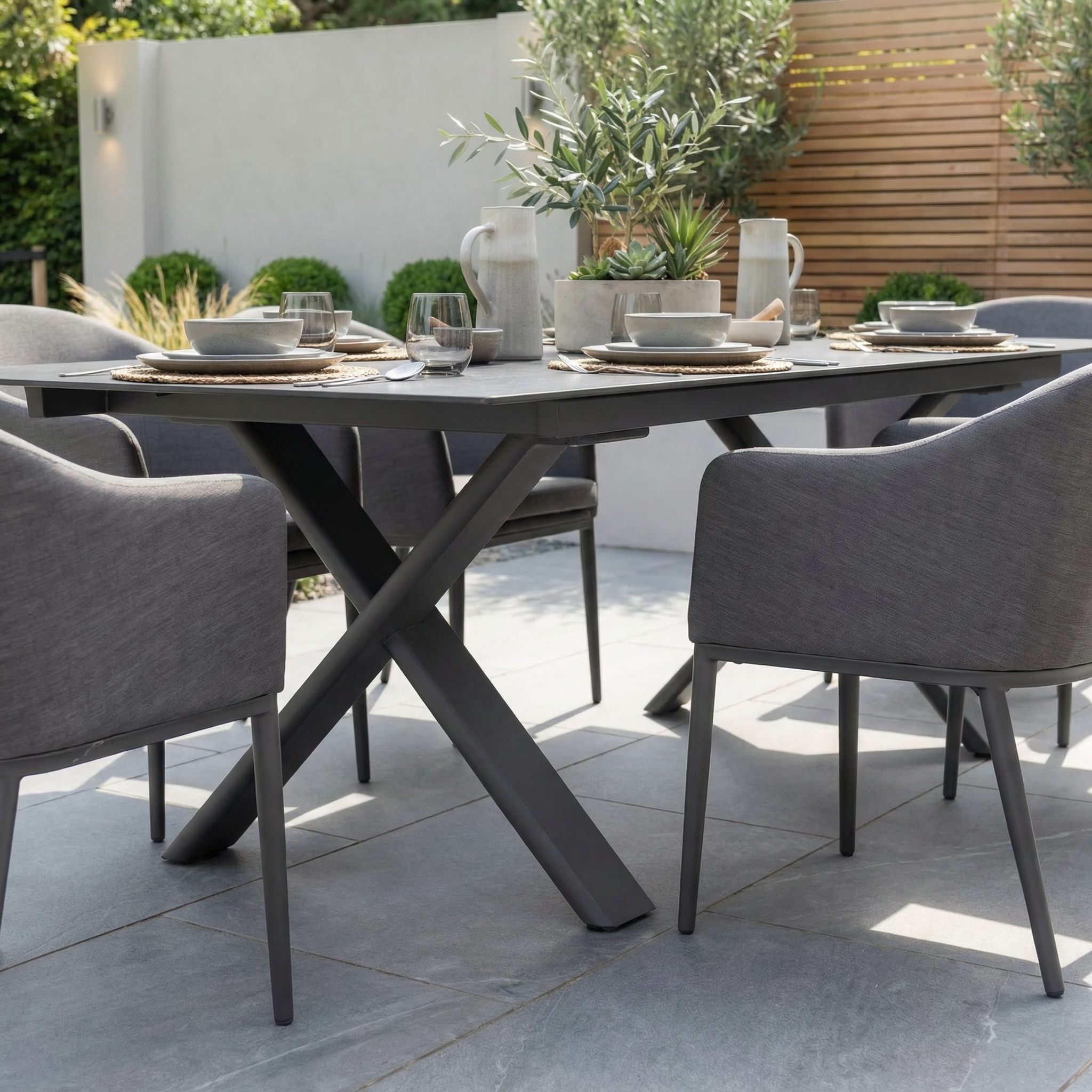 The Luna 6 Seat Outdoor Fabric Dining Set with Albatross Extending Table in Grey features stylish all-weather chairs and a spacious table, perfect for outdoor dining with plates, glasses, and a plant centerpiece on your patio.