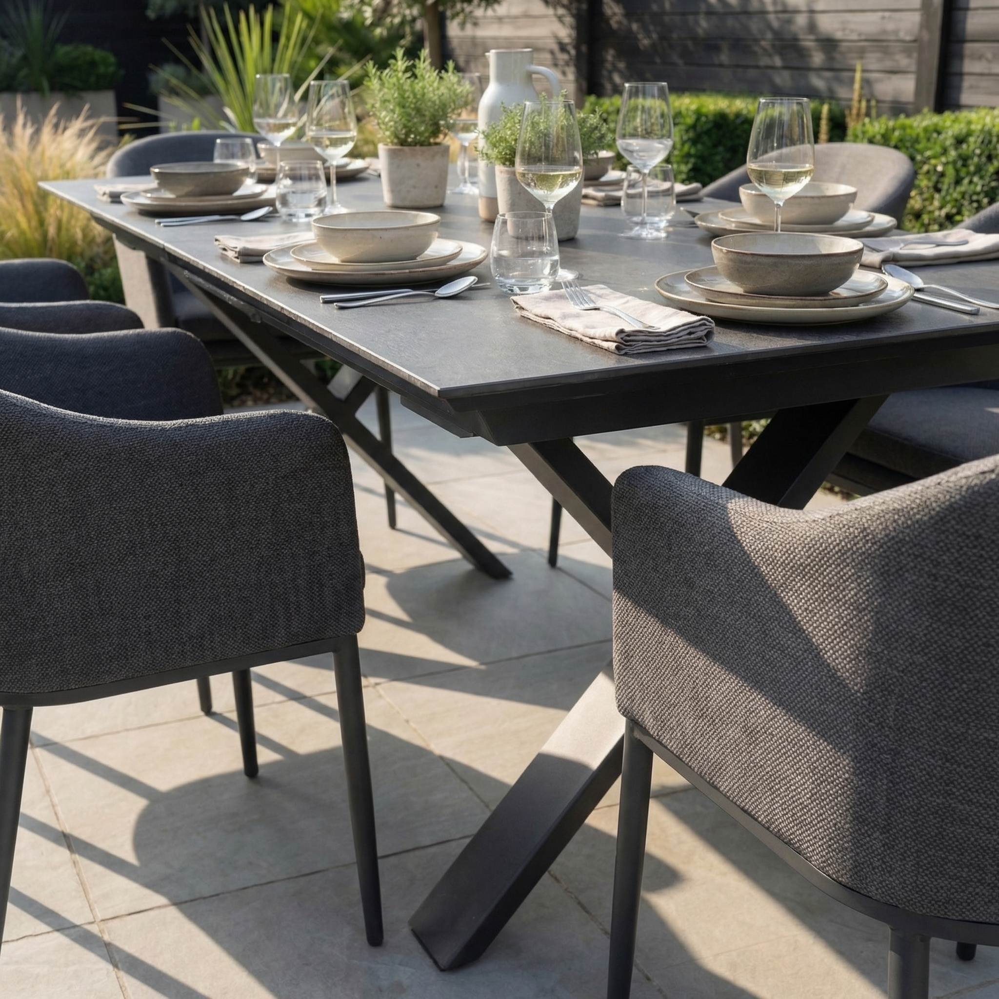 The Luna 6 Seat Outdoor Fabric Dining Set with Albatross Extending Table in Grey features all-weather chairs, gray plates, glasses, and napkins elegantly arranged for dining.