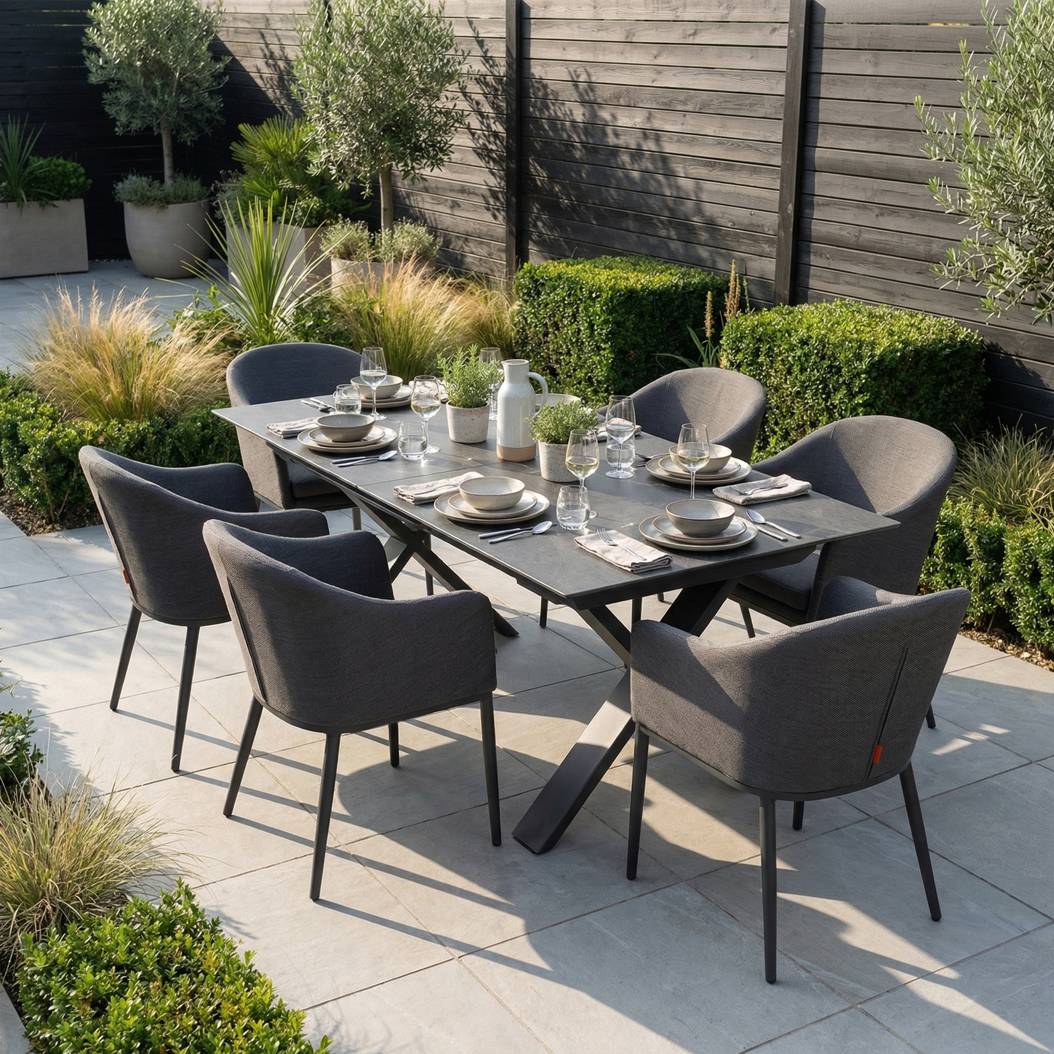 The Luna 6 Seat Outdoor Fabric Dining Set with Albatross Extending Table in Grey features six all-weather chairs and a rectangular table, perfect for outdoor dining surrounded by greenery.